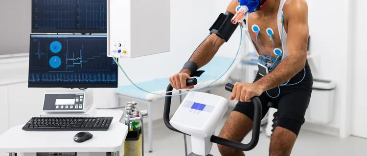 A man undergoing a fitness test on a stationary exercise bike, connected to medical monitoring equipment.