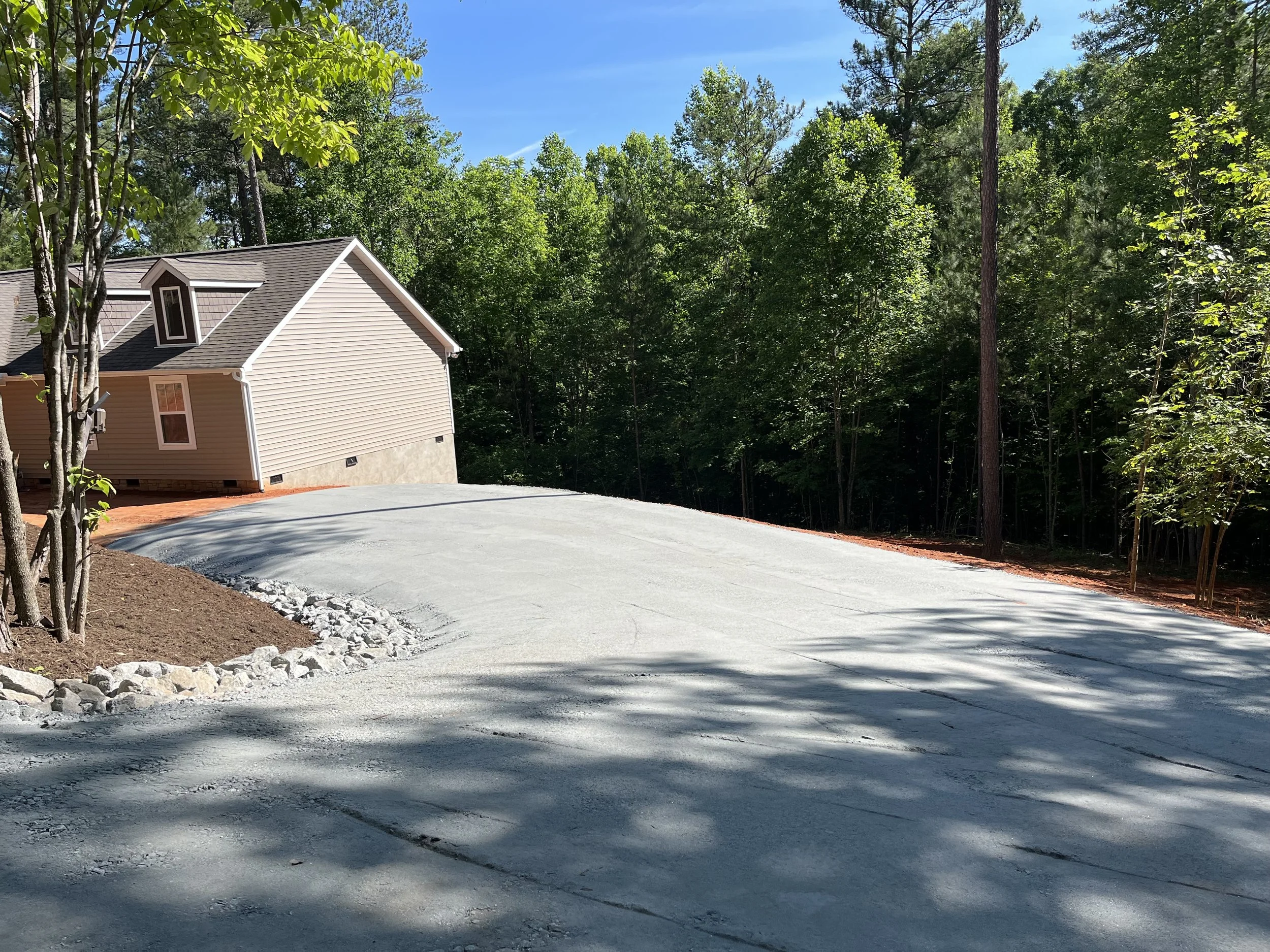 Newly paved driveway leading to a house in a wooded area with tall trees and clear blue sky