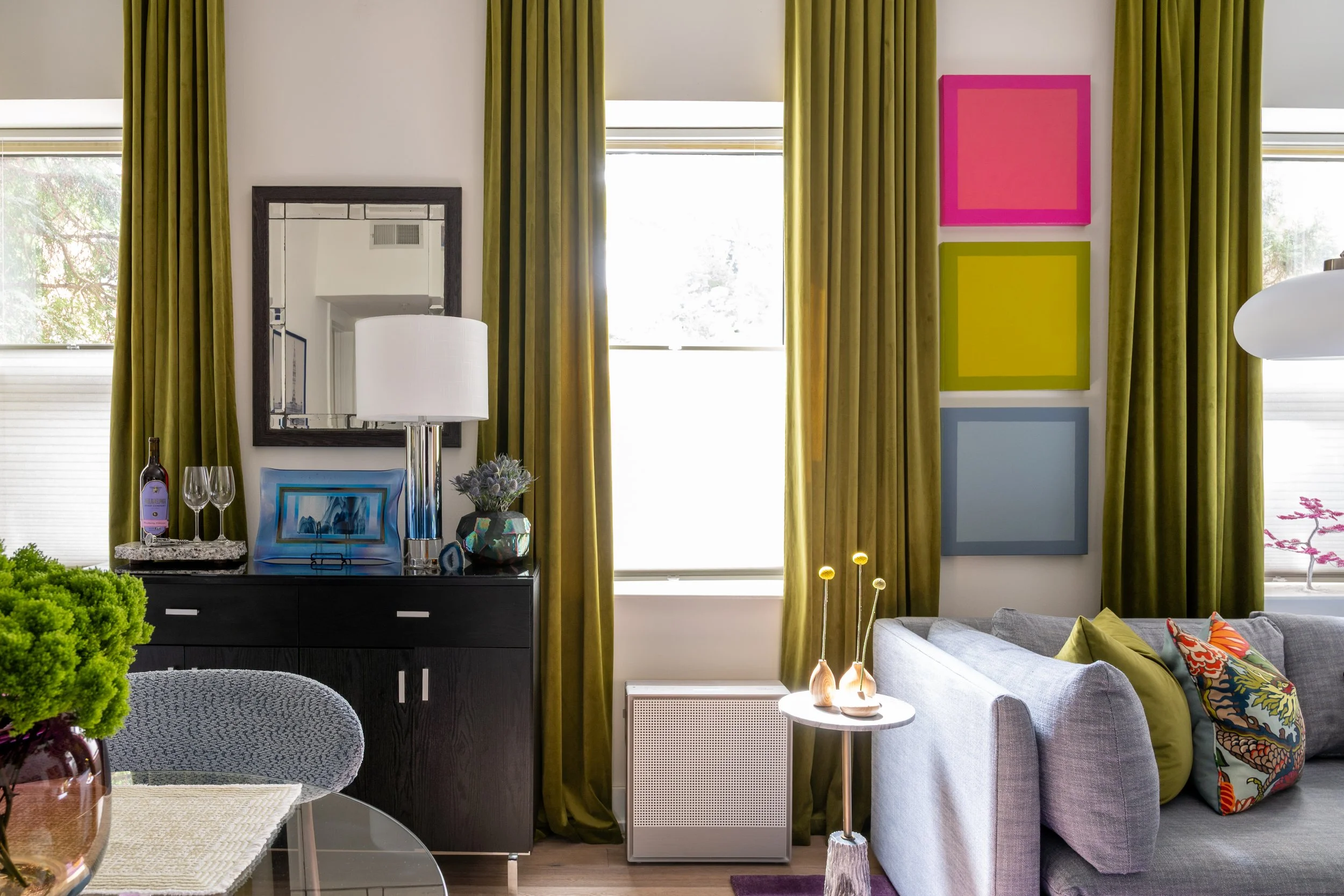 Eclectic Old City Philadelphia living room with olive green velvet curtains, colorful art, and gray sofa.