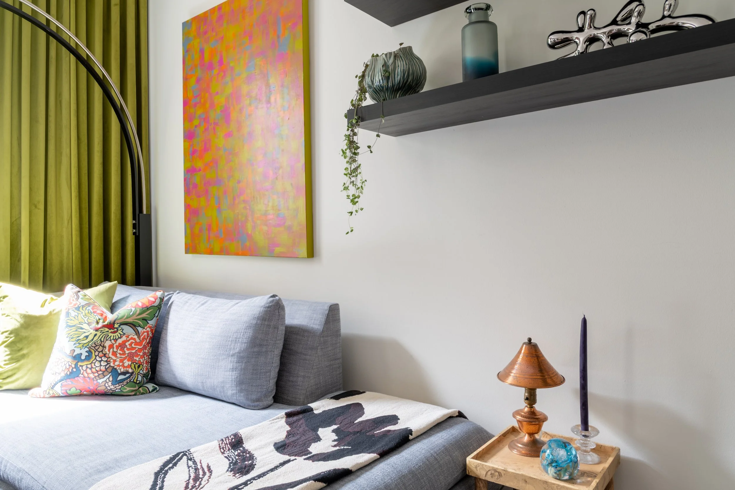 Eclectic Philadelphia living room design with colorful abstract art, floating shelves, and gray chaise sofa.