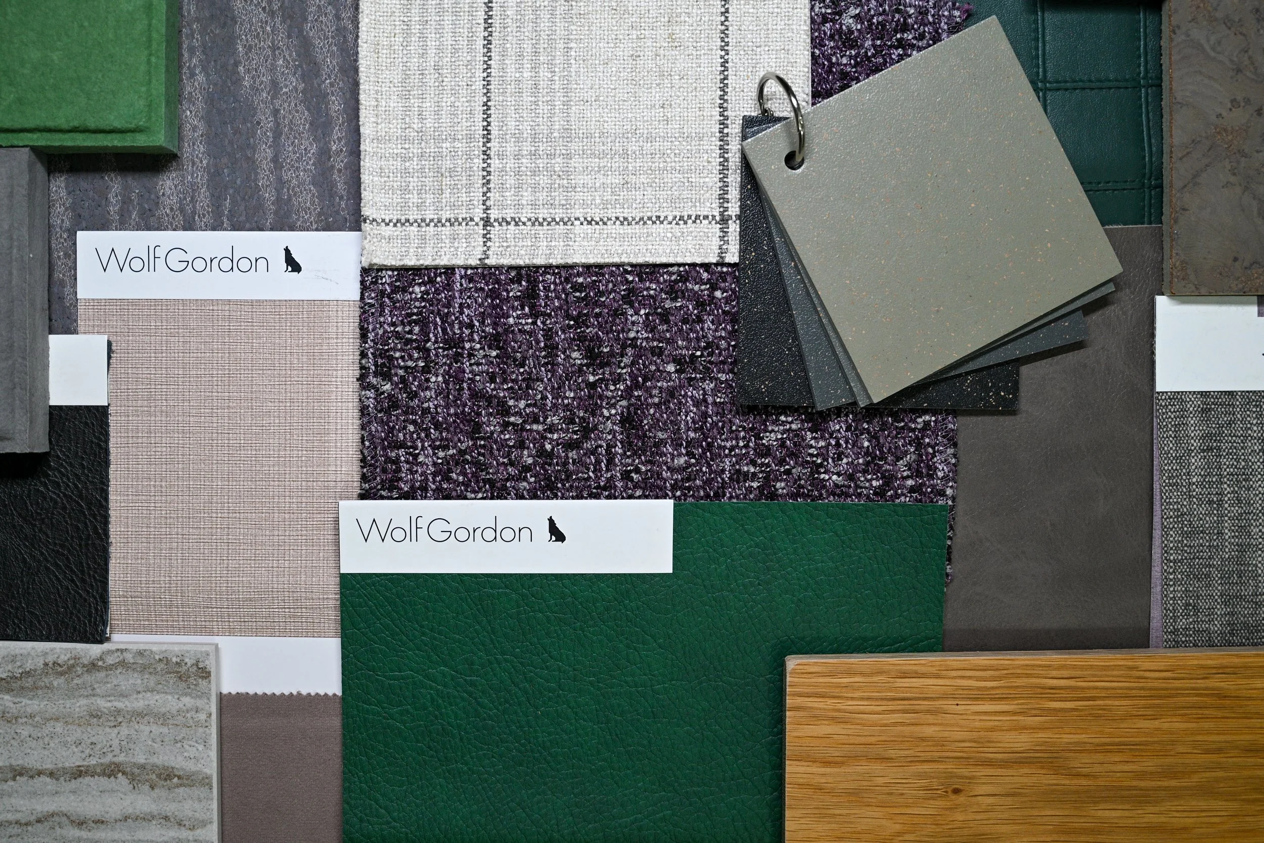 Flat lay of curated interior design material samples:  textiles, leather, wood, and wallcoverings from Wolf Gordon, showcasing a neutral and green palette used for timeless, sustainable residential interior design by a Philadelphia Interior Designer.