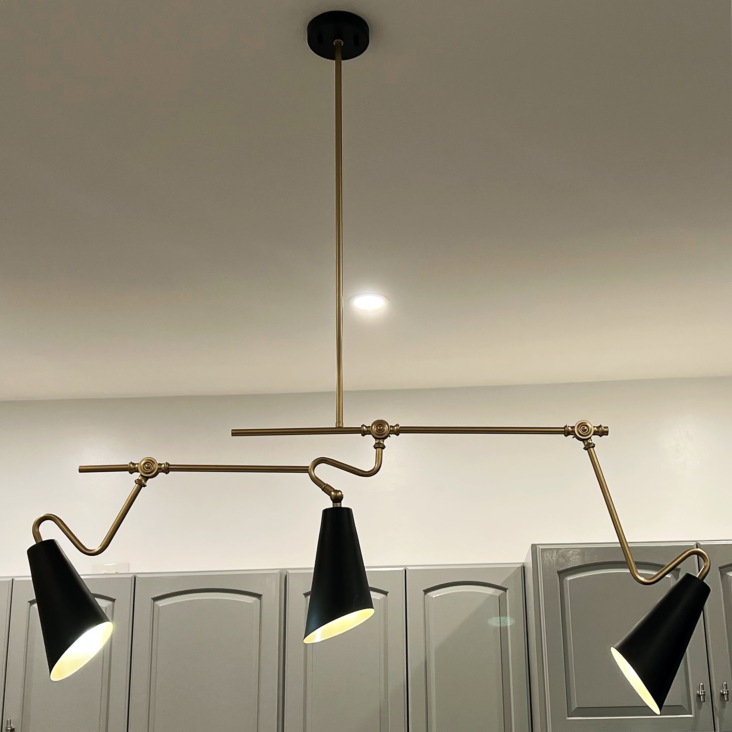 Detail of modern black-and-brass pendant lighting above kitchen island and gray cabinetry — Corning Apartment 101.