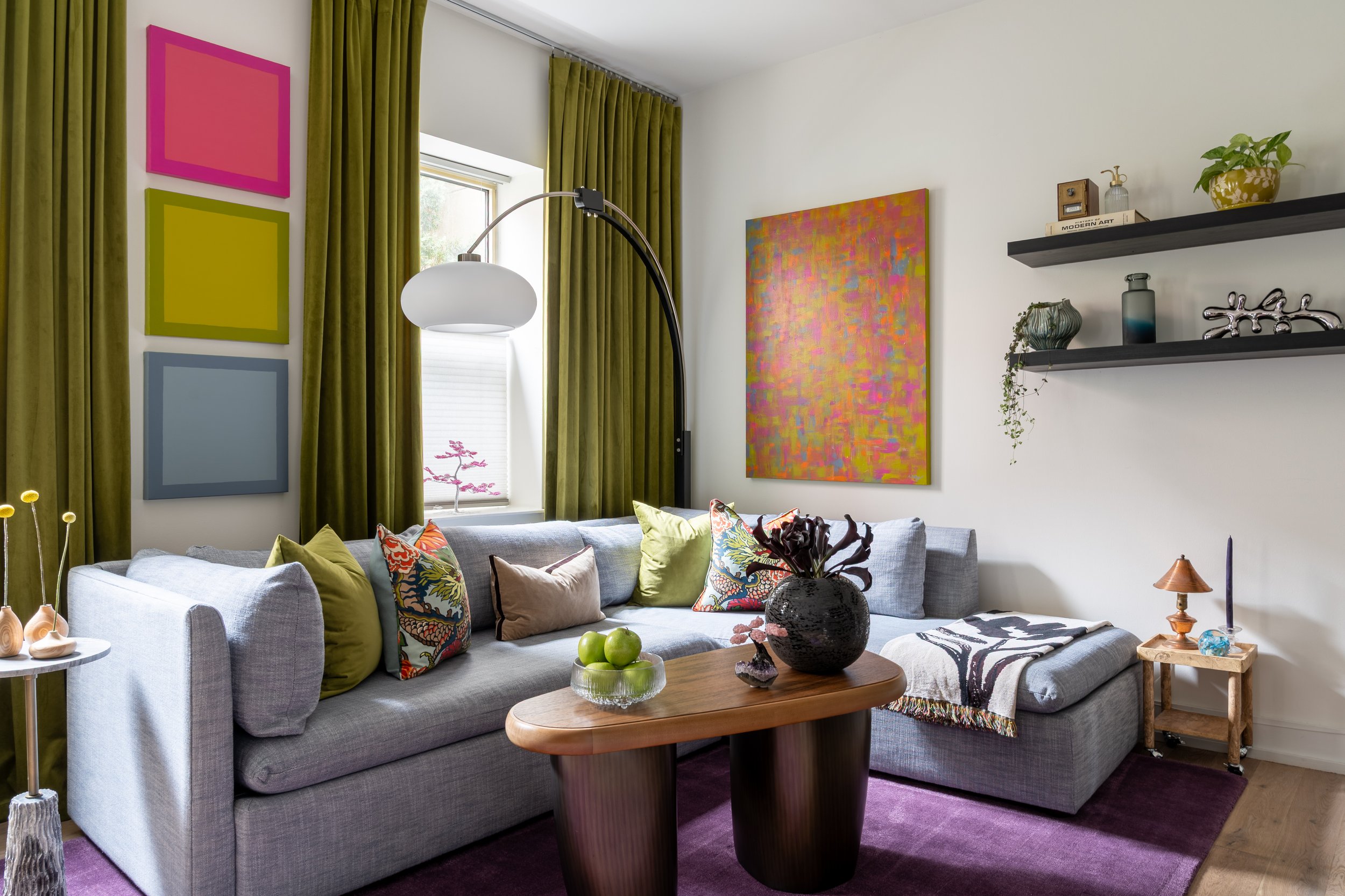 Eclectic living room design in Old City Philadelphia with colorful artwork, green curtains, and gray sectional.
