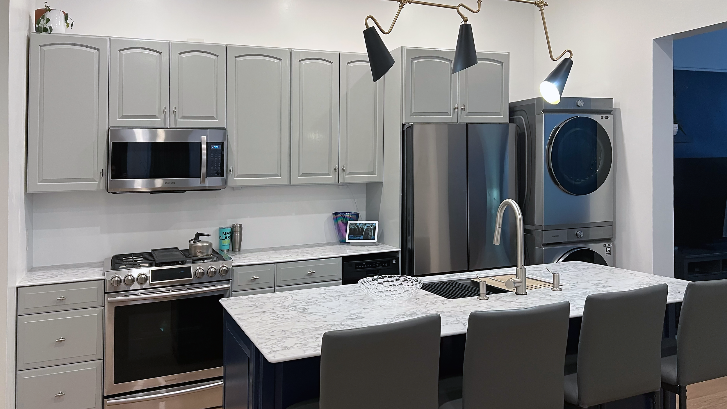 Wide view of kitchen showing gray cabinets, stainless steel appliances, and marble-look countertops in Corning Apartment 101.
