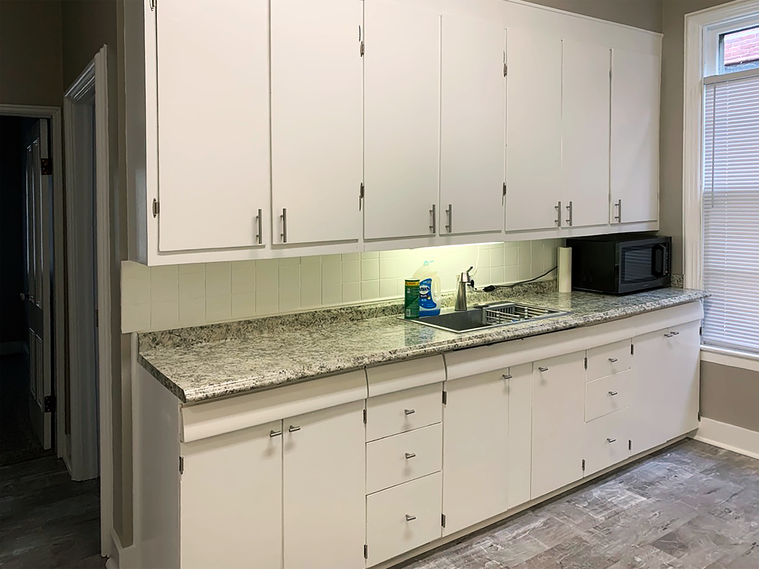 Updated galley kitchen with white cabinets, granite-like countertops, and modern lighting.