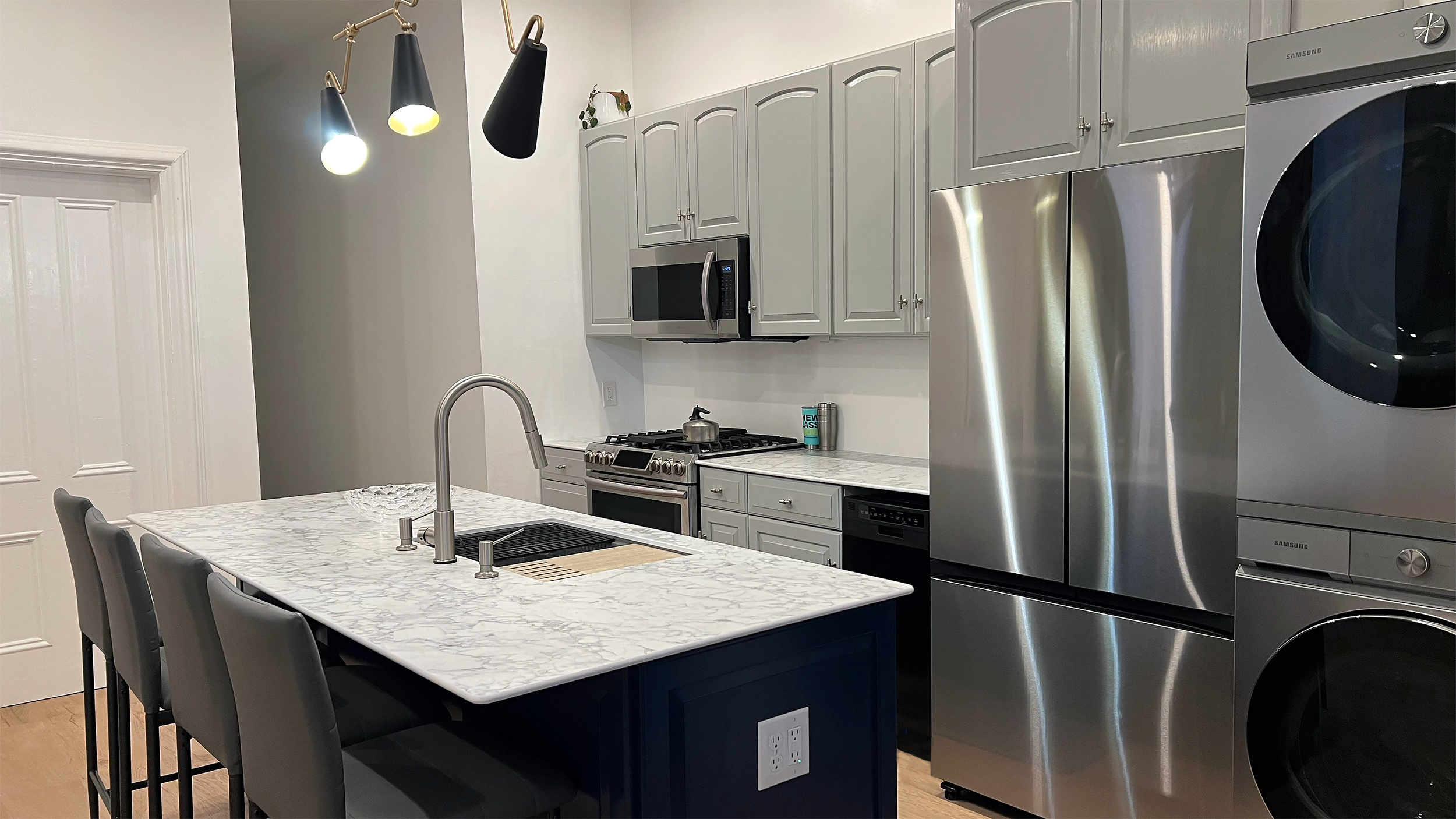 Detail of modern black-and-brass pendant lighting above kitchen island and gray cabinetry — Corning Apartment 101.