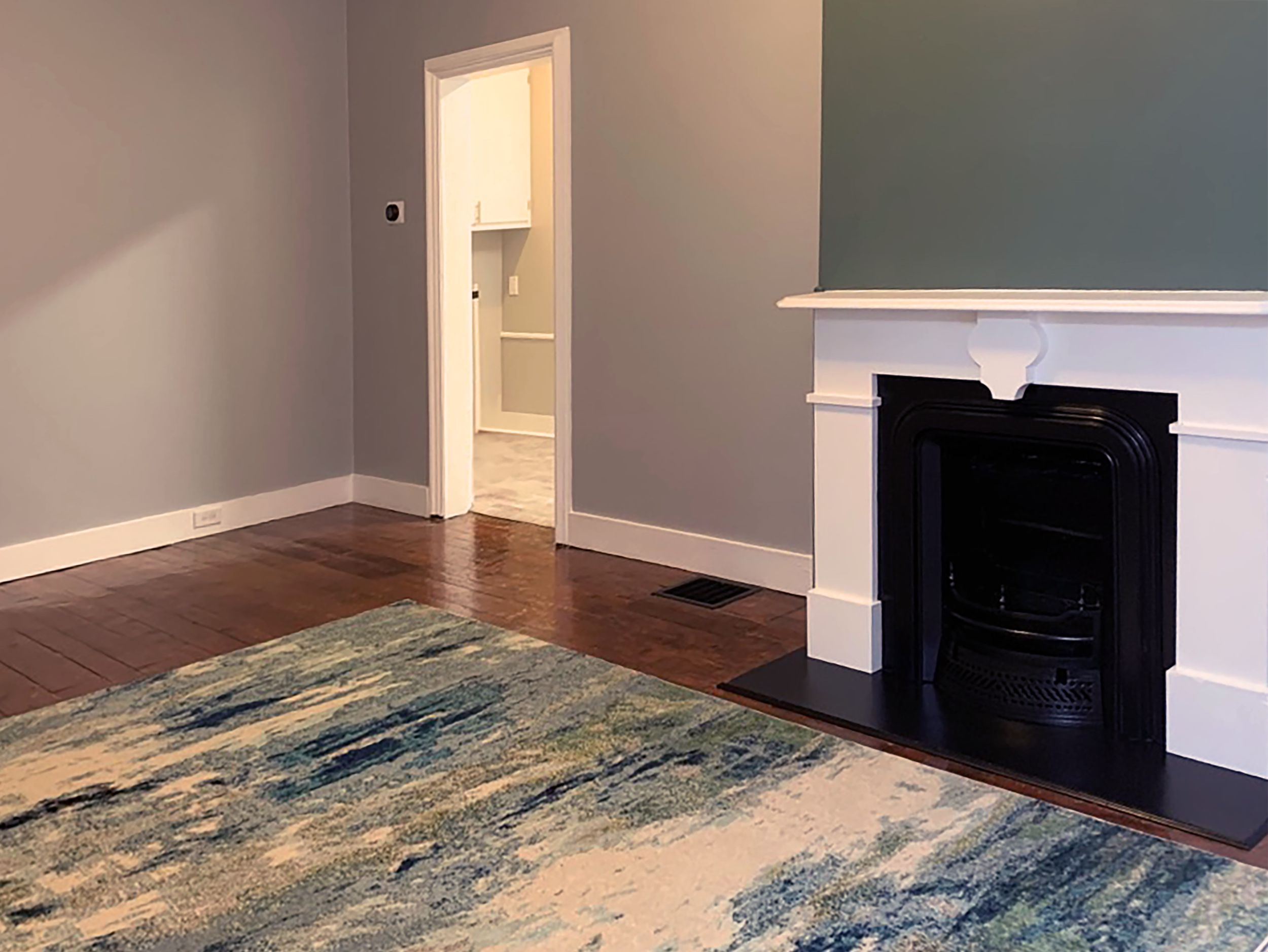 Restored living room with historic fireplace, green accent wall, hardwood floors, and blue-green area rug