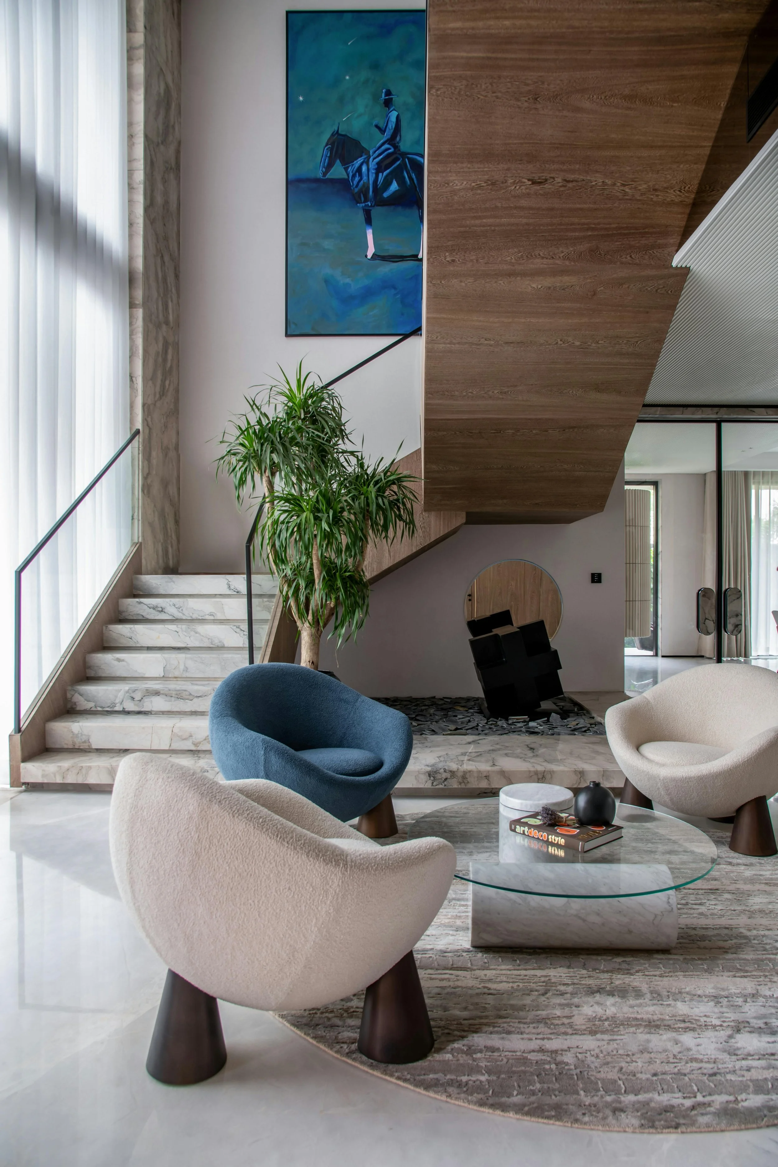 Luxury living room with sculptural chairs, marble staircase, and curated art, showcasing contemporary interior design.