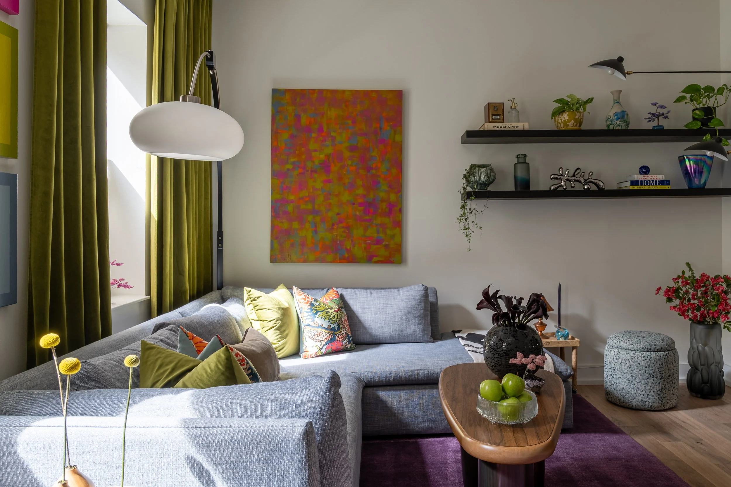 Eclectic Old City Philadelphia living room design with gray sectional, colorful art, and floating shelves.