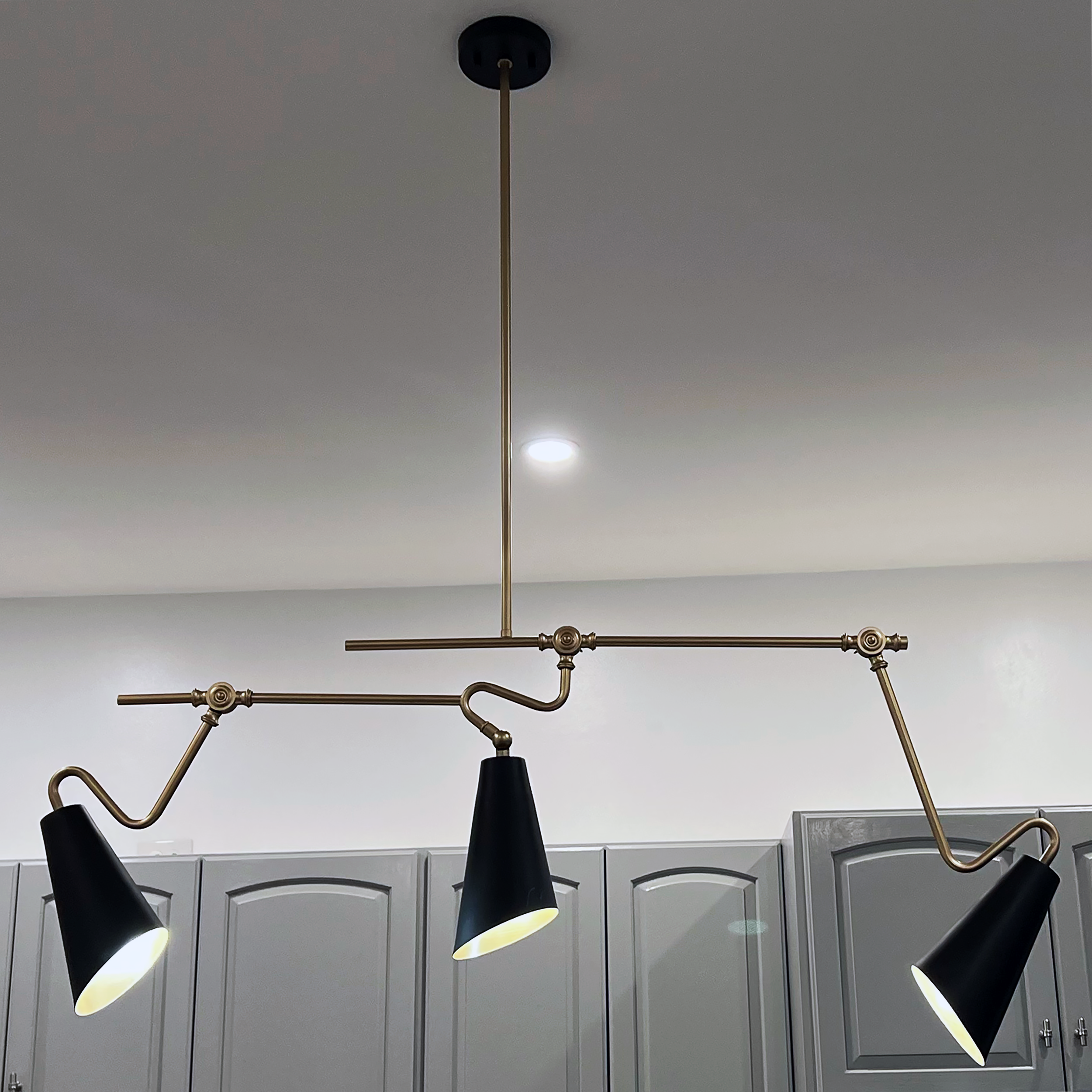 Detail of modern black-and-brass pendant lighting above kitchen island and gray cabinetry — Corning Apartment 101.
