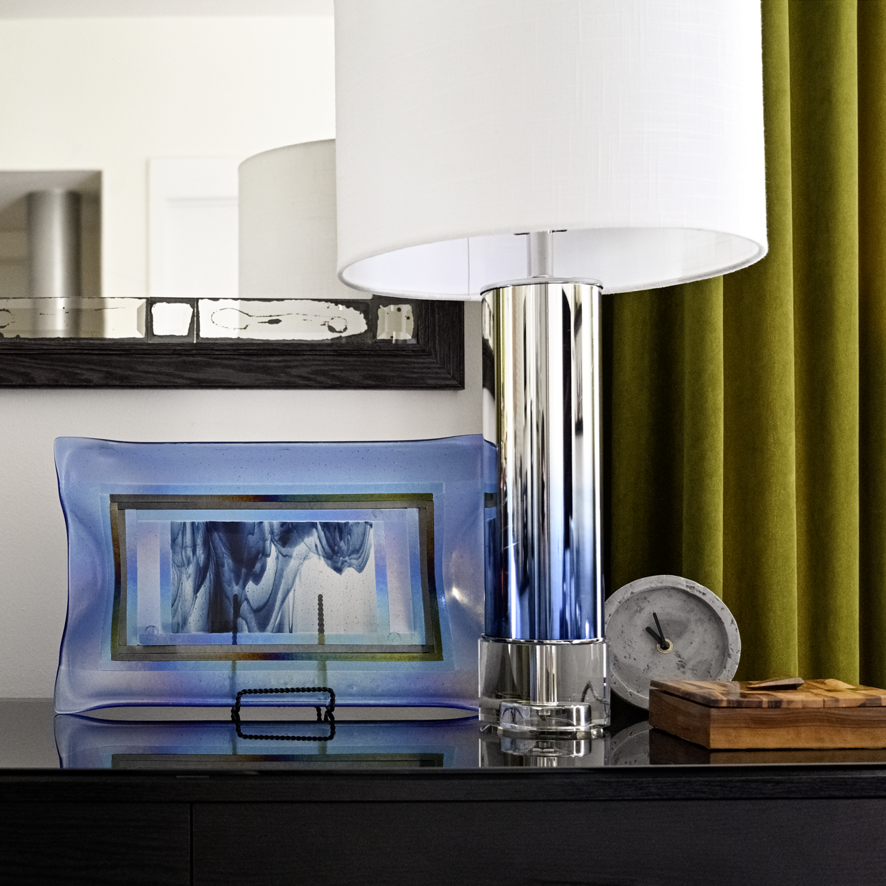Luxury interior design vignette in a Philadelphia apartment featuring olive green velvet drapery, a chrome table lamp, granite tray bar setup, and layered modern decor within a historic building.