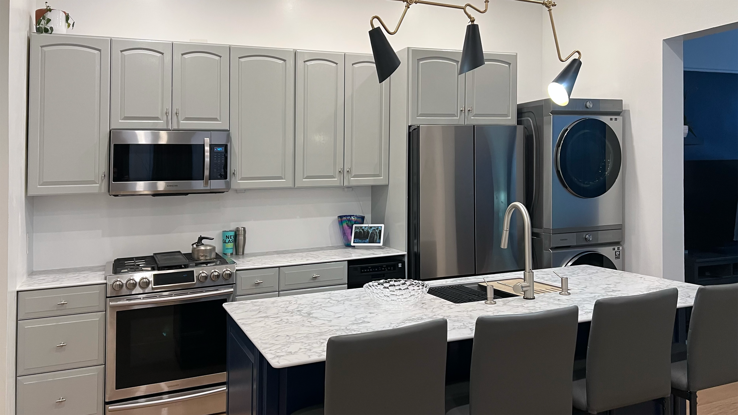 Wide view of kitchen showing gray cabinets, stainless steel appliances, and marble-look countertops in Corning Apartment 101.