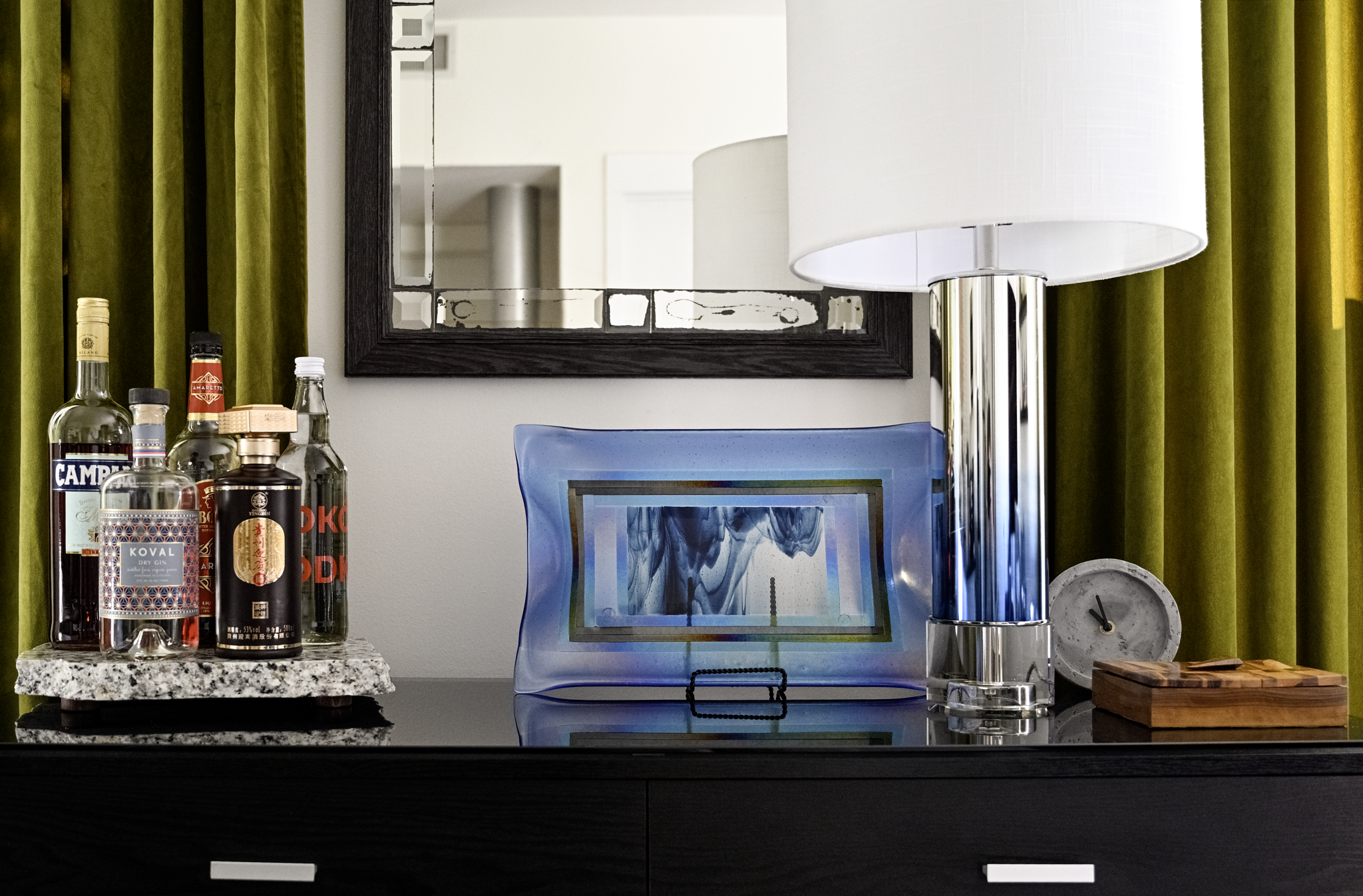 Luxury interior design vignette in a Philadelphia apartment featuring olive green velvet drapery, a chrome table lamp, a granite tray bar setup, and layered modern decor within a historic building.