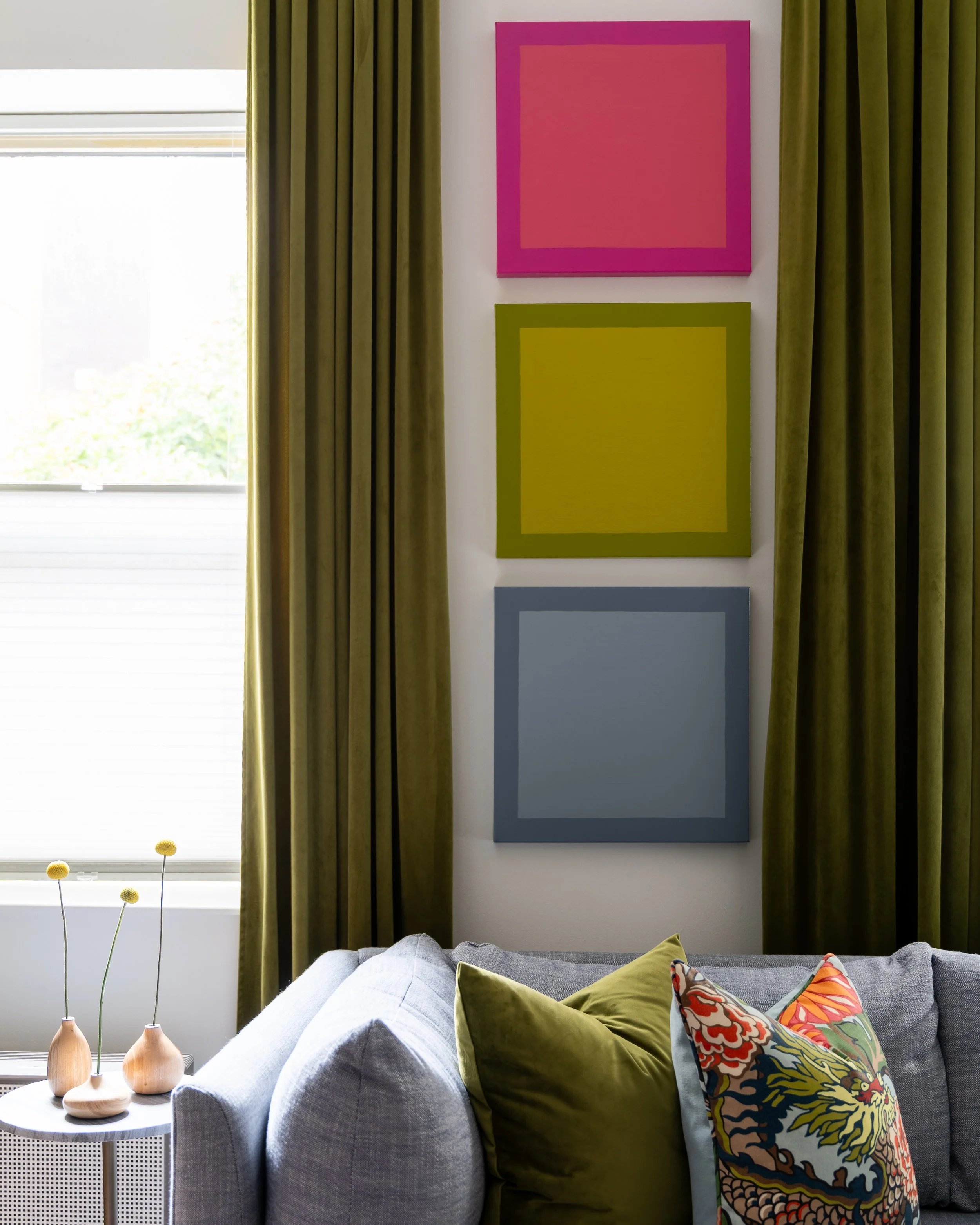 Colorful wall art, olive green curtains, and patterned pillows in an eclectic Old City Philadelphia living room.