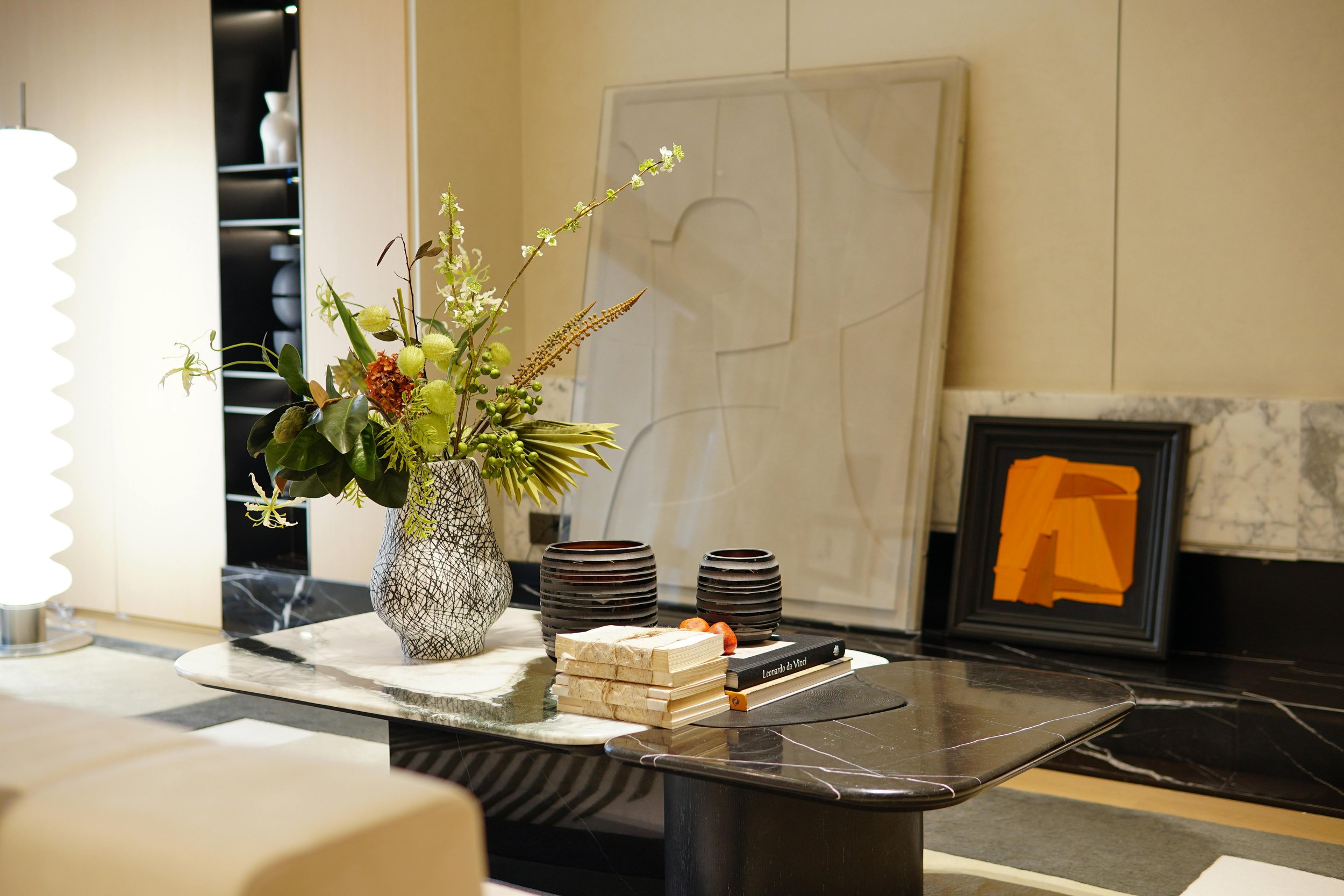 Modern coffee table styled with a sculptural vase, greenery arrangement, stacked books, and contemporary artwork in a curated living space.