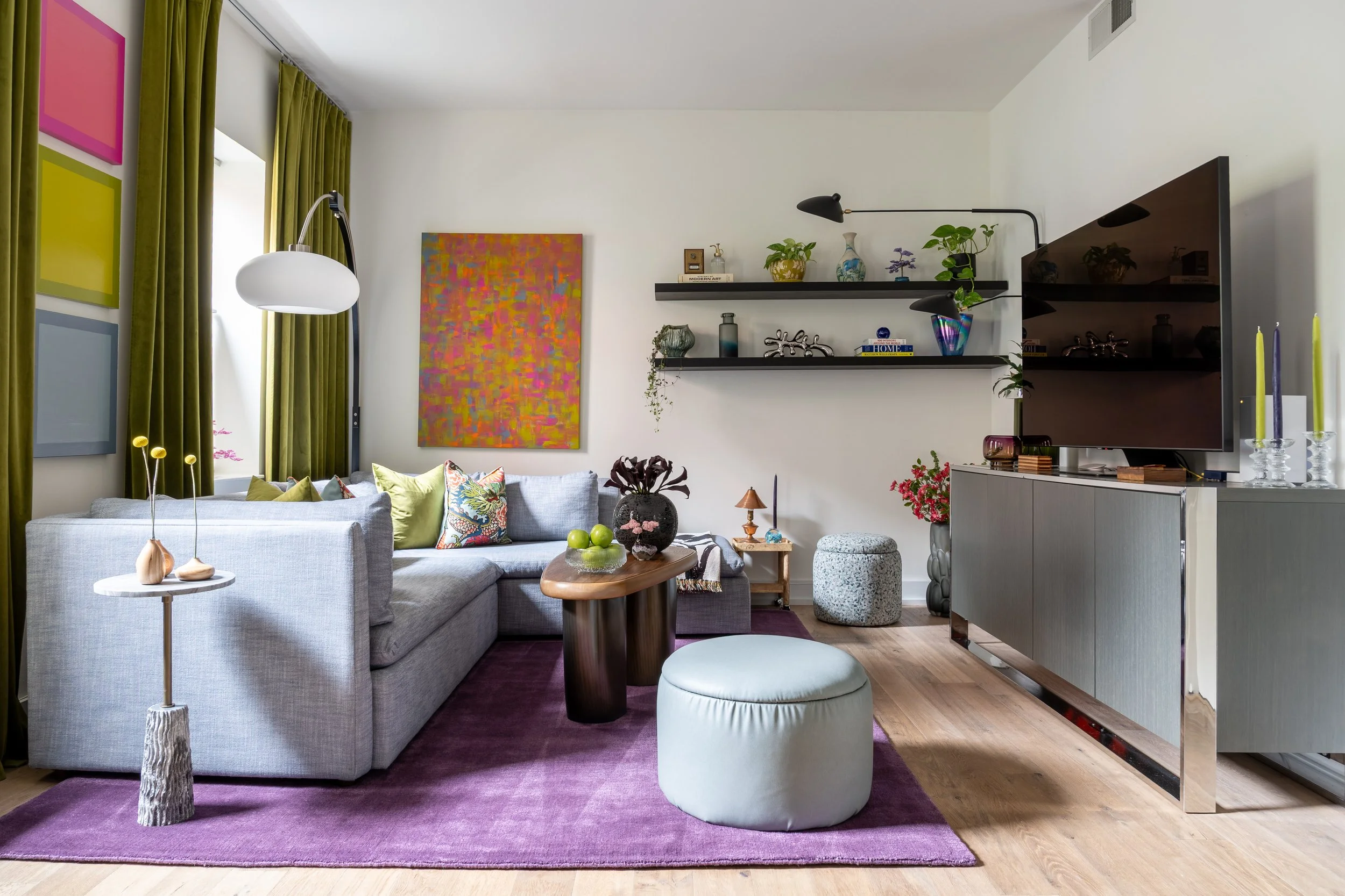 Eclectic Old City Philadelphia living room design with gray sectional, purple rug, colorful art, and green curtains.