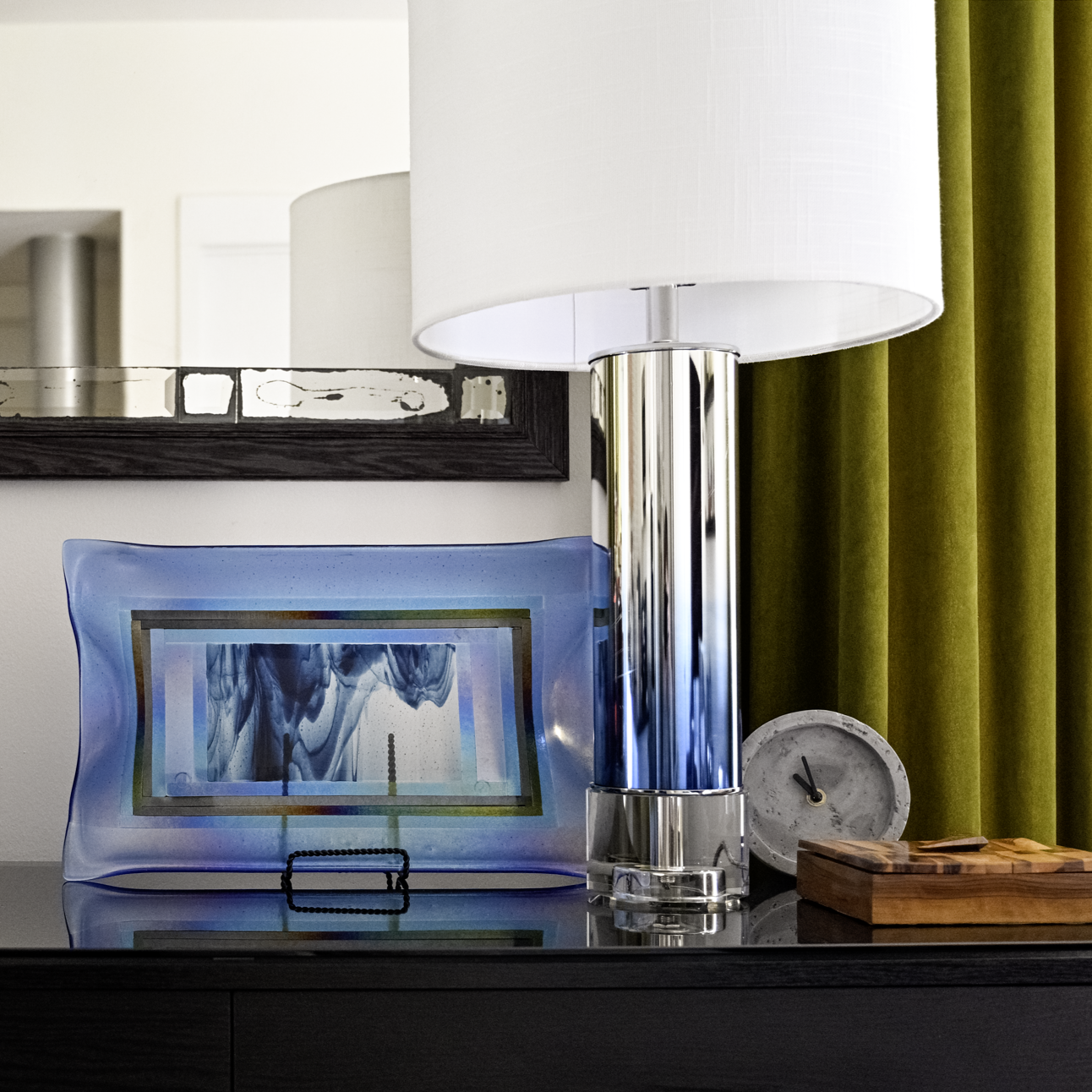 Luxury interior design vignette in a Philadelphia apartment featuring olive green velvet drapery, a chrome table lamp, granite tray bar setup, and layered modern decor within a historic building.