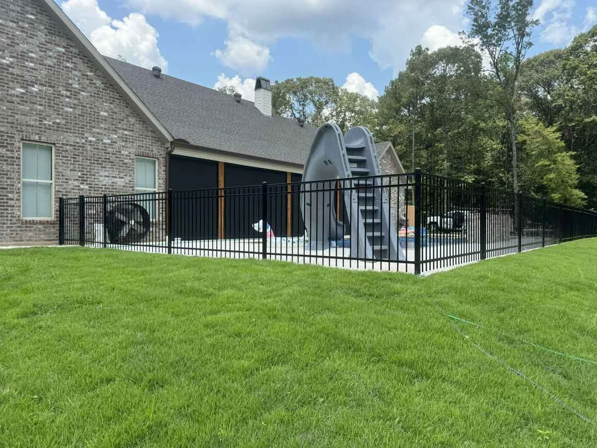 A house and pool with a slide surrounded by a fence from Alexandria, LA Pro-Mow landscape company.