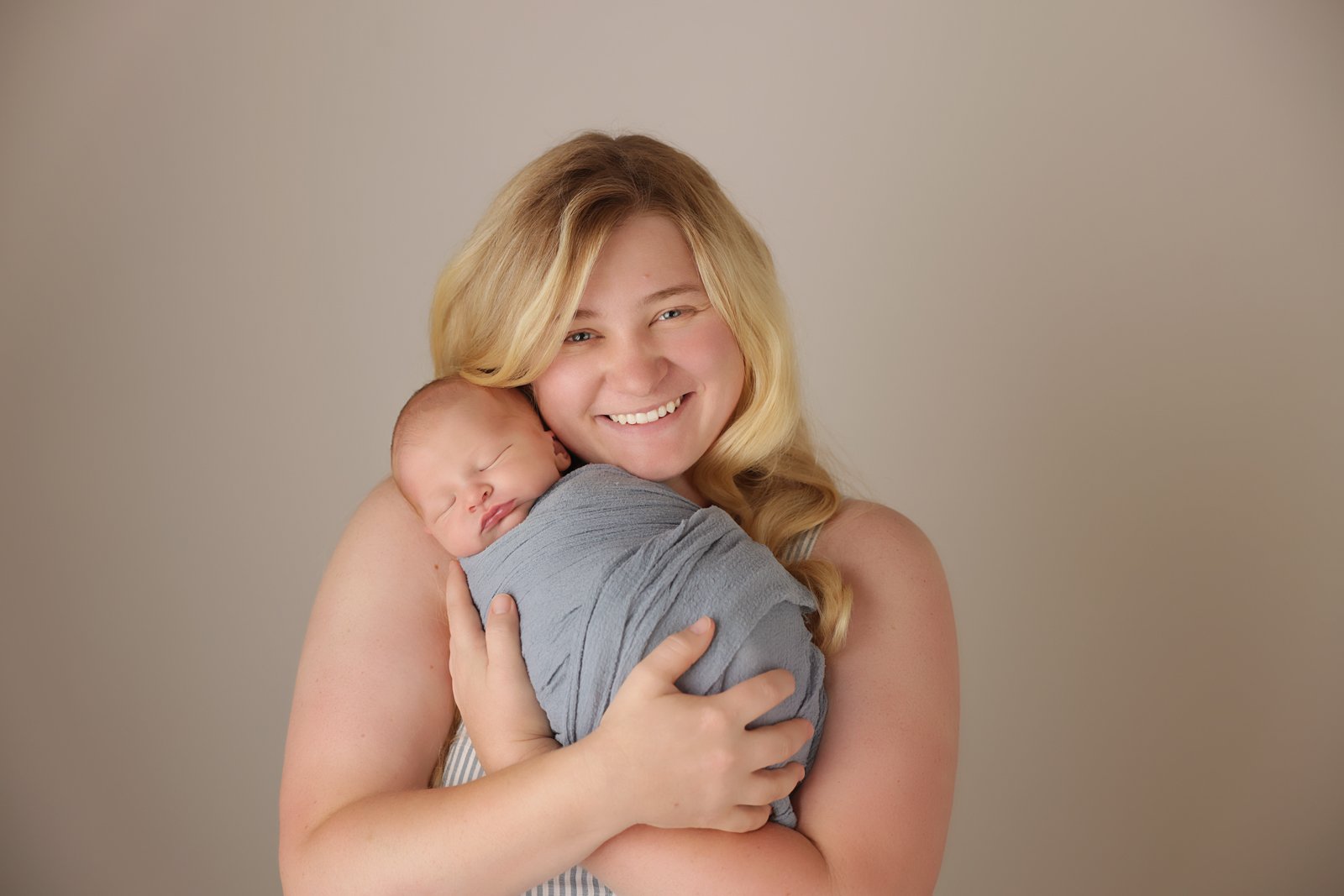 Hannah Bower's headshot, with long blonde hair smiling and holding a sleeping newborn wrapped in a gray blanket.