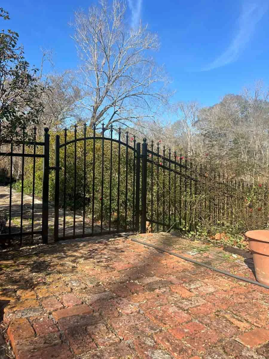 A patio and fence built by Alexandria, LA Pro-Mow landscaping company, in front of green shrubbery.
