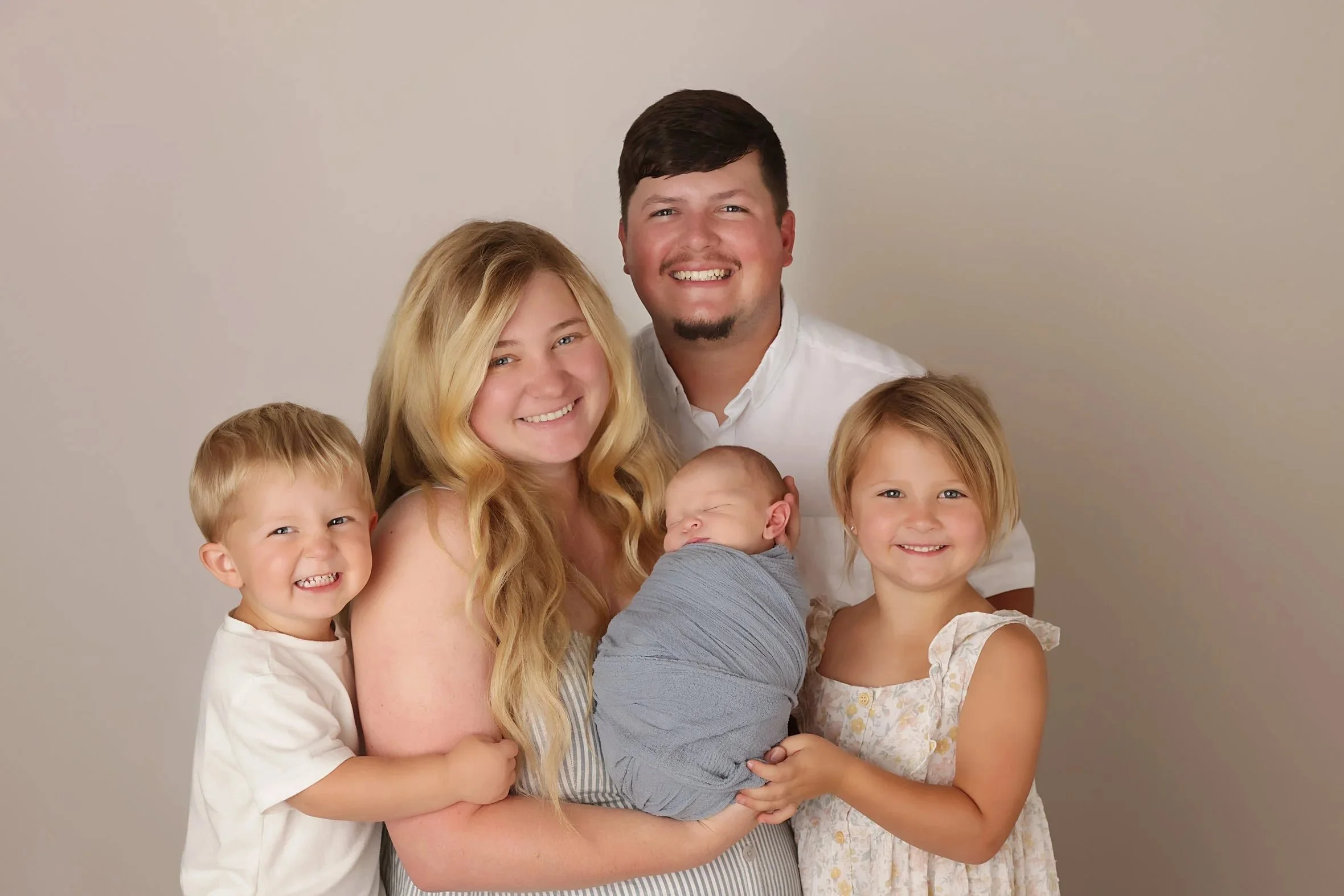 Garrett Bower's family of five with two adults and three children. The picture includes a baby, smiling and posing together against a neutral backdrop.