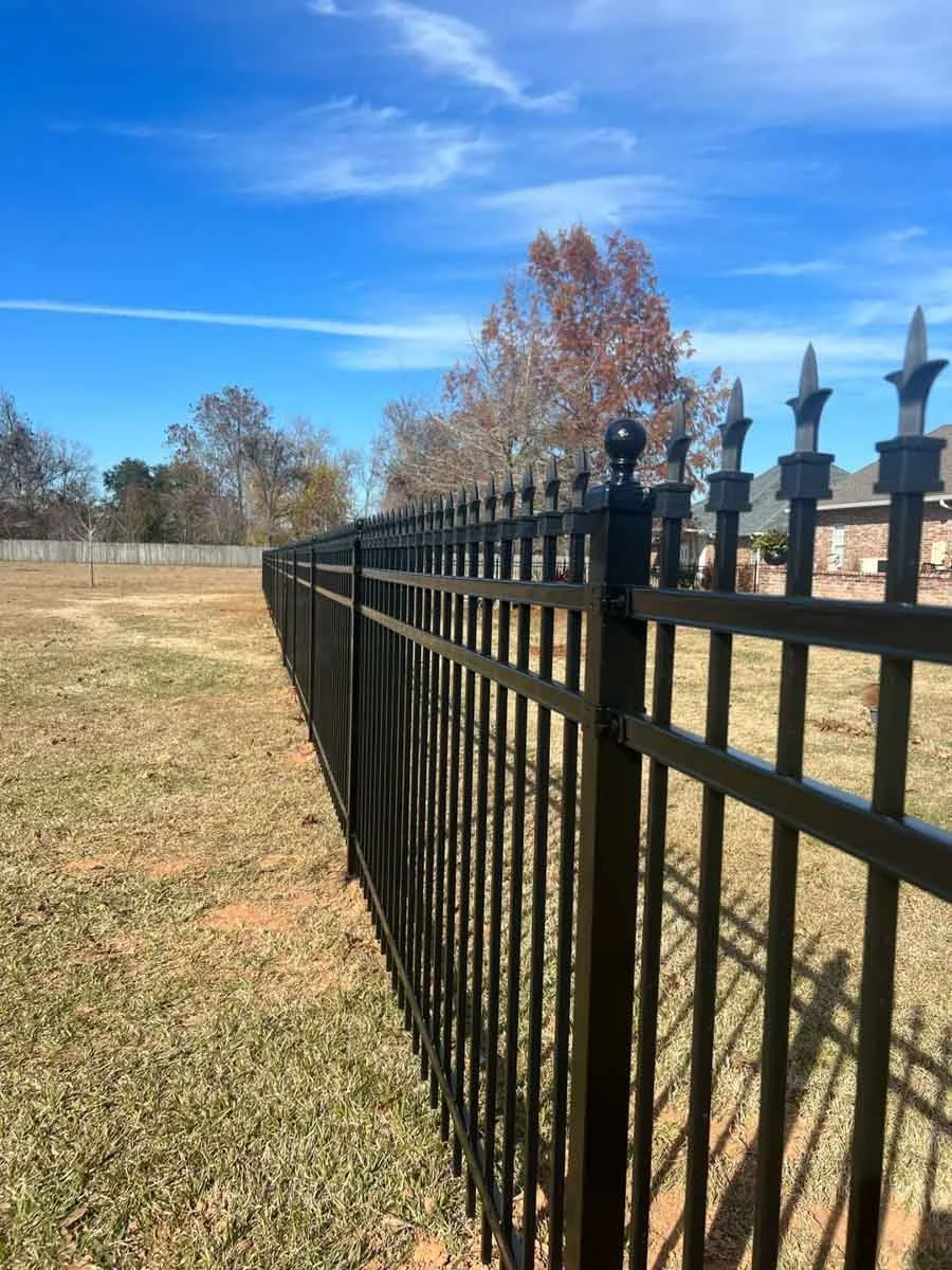 Alexandria, LA Pro-Mow landscape company's metal fence in a yard under a blue sky with red trees.