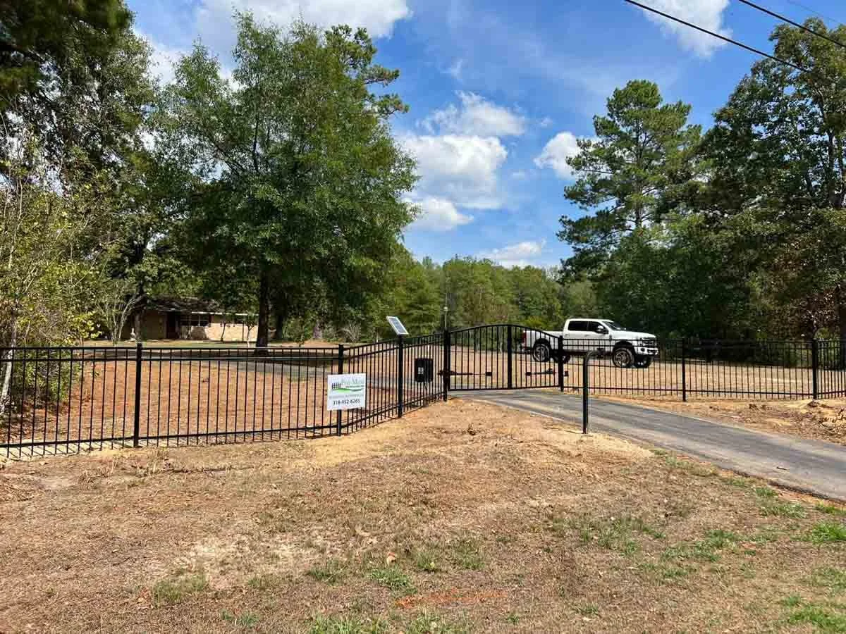 A field with an iron fence, trees, and a white pick-up truck in the background.