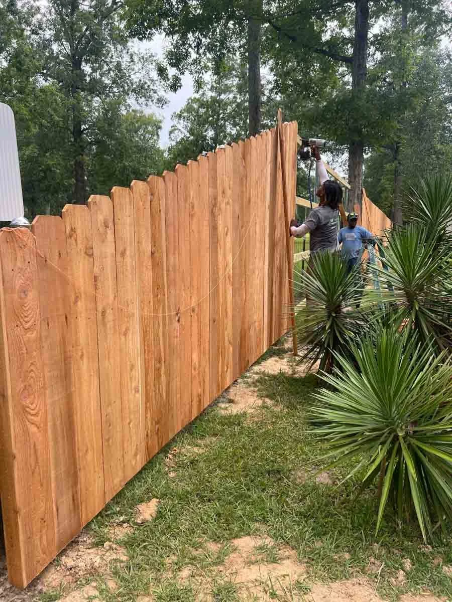 Alexandria, LA Pro-Mow landscape company installing a wooden fence with trees and shrubbery behind.
