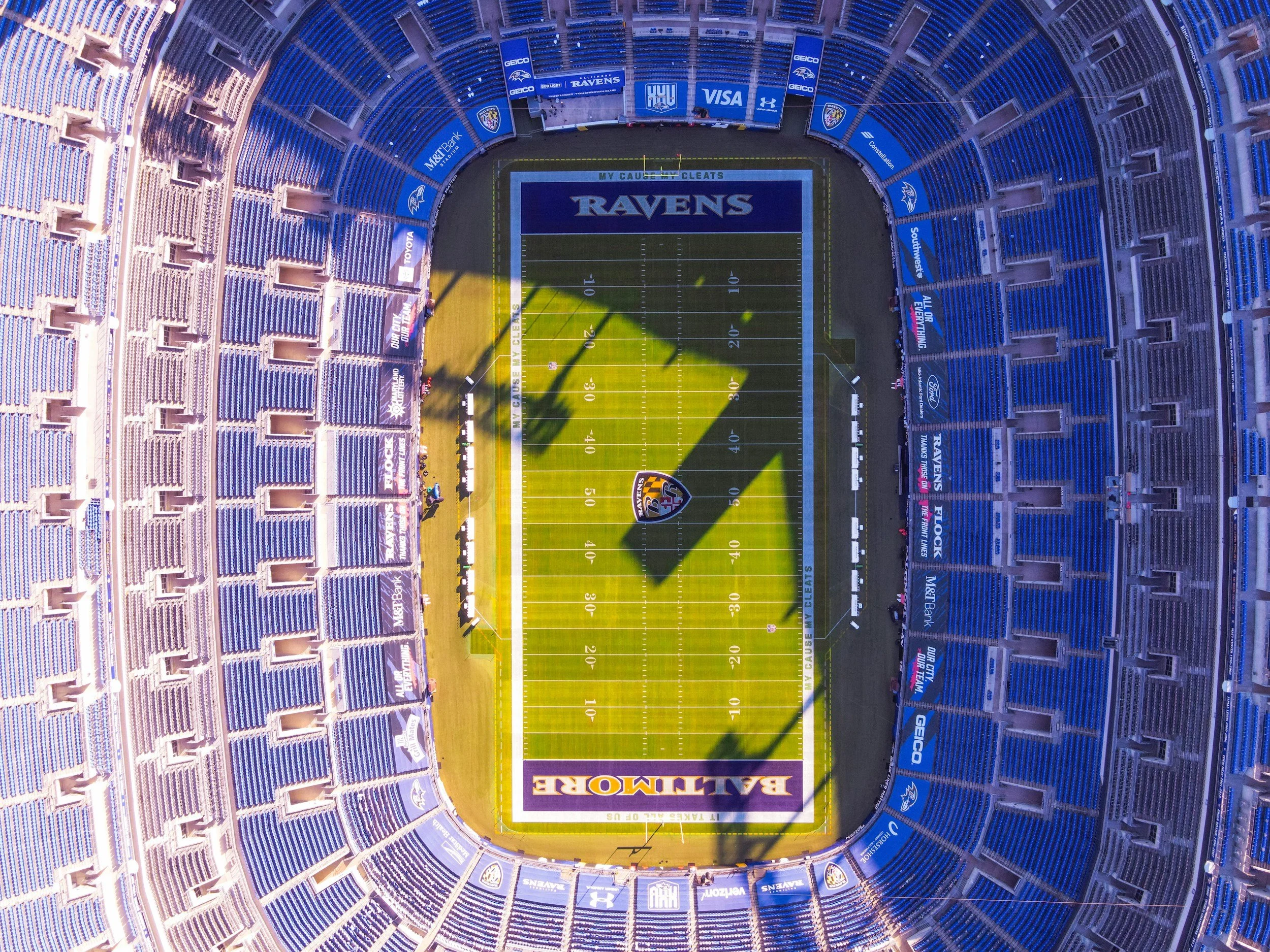 Aerial view of M&T Bank Stadium in Baltimore, Maryland, showcasing the football field with the Baltimore Ravens logo, seating areas with blue seats, and advertising banners around the stadium.