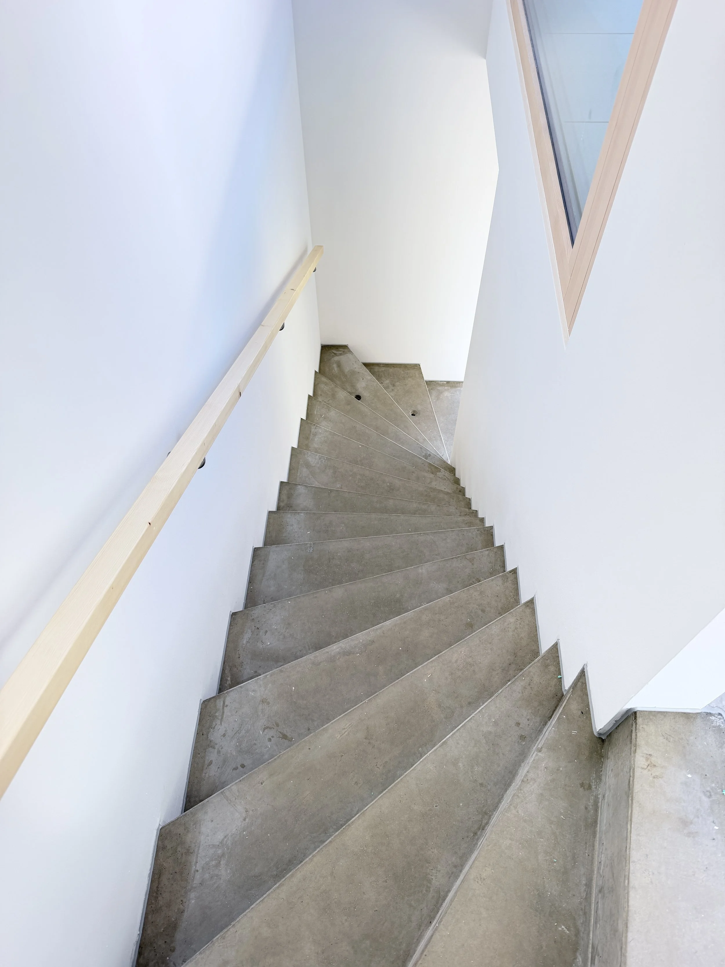Ein gerader Treppenabsatz mit grauen Steintreppen, weißen Wänden und einem großen Dachfenster, das Tageslicht hereinlässt.