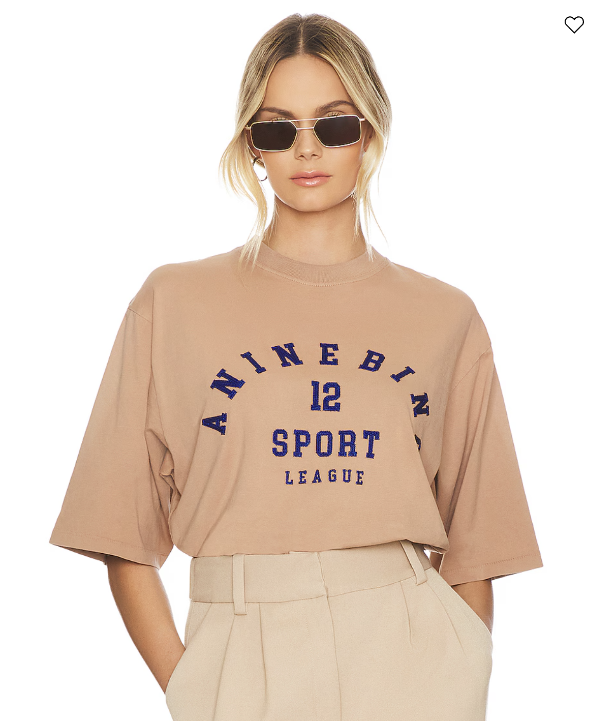 A woman wearing sunglasses and a beige oversized T-shirt with blue text that says "A NINE B I N 12 SPORT LEAGUE" stands against a white background.