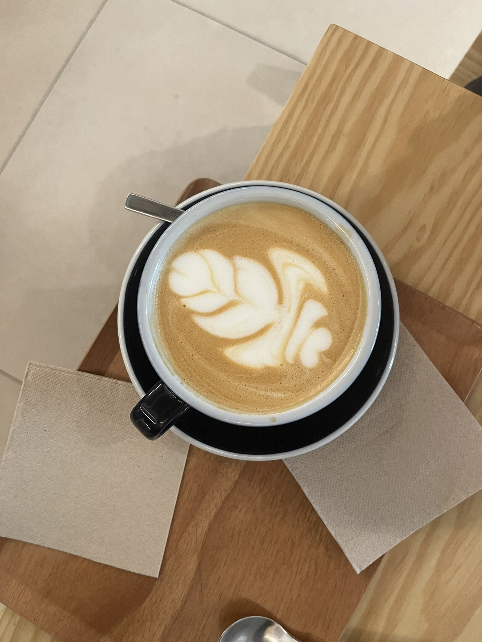 Una taza de café con arte de leche en forma de corazón y hojas, sobre una mesa de madera.