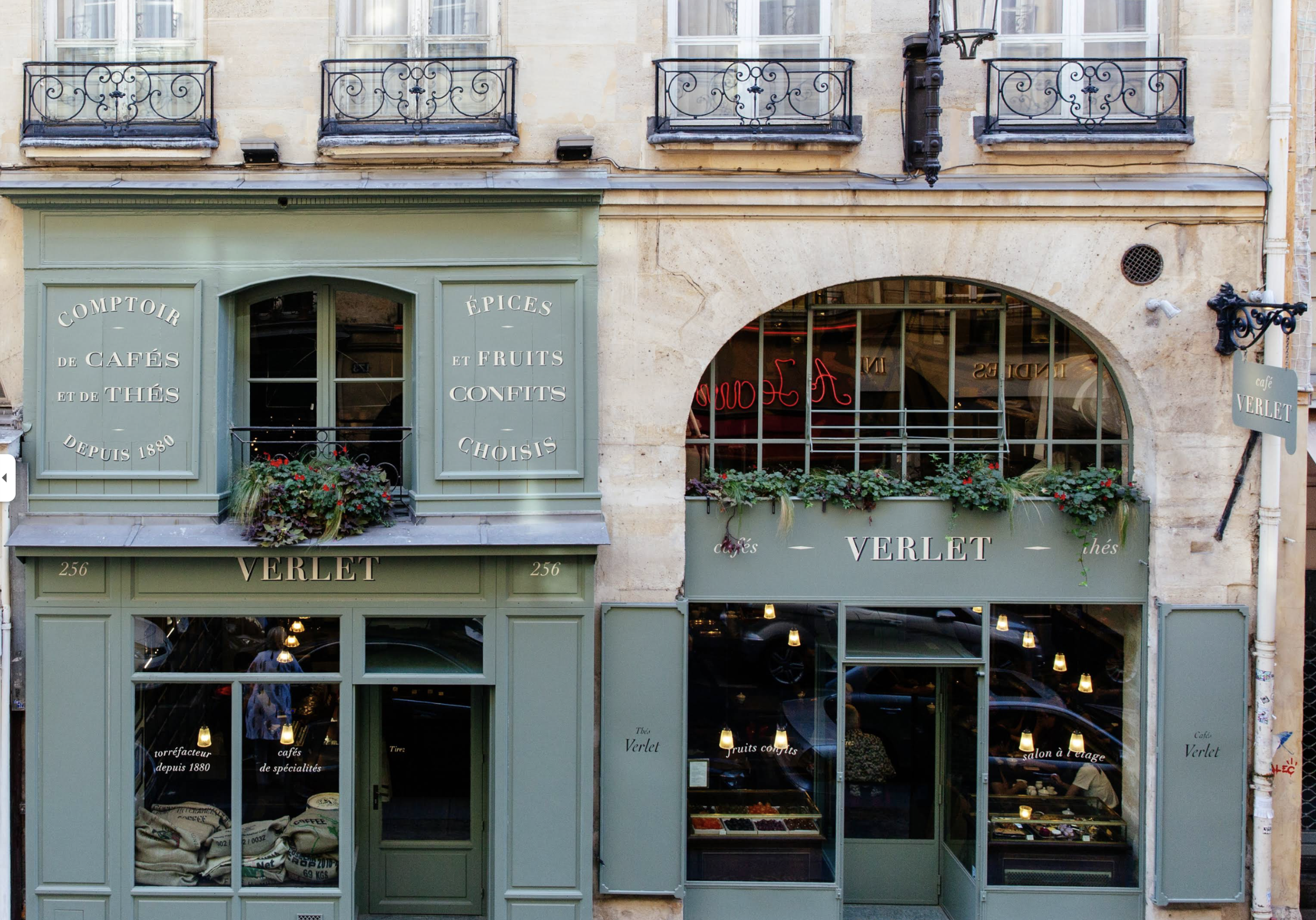 Fachada de la cafetería  Parisina' Verlet'. Fachada de color verde con ventanas grandes y un letrero con el nombre de la tienda. Ventanas con plantas y decoraciones, y un cartel lateral con el mismo nombre.