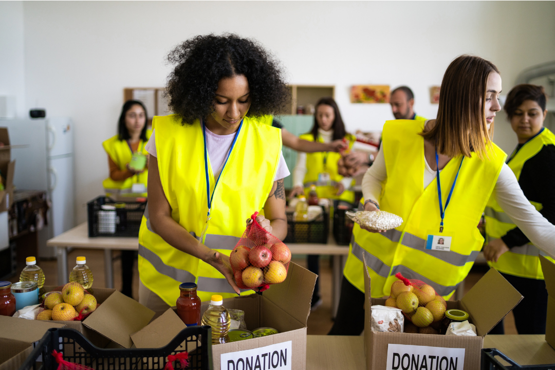 Group of volunteers wearing yellow safety vests packing food donations in a community center.