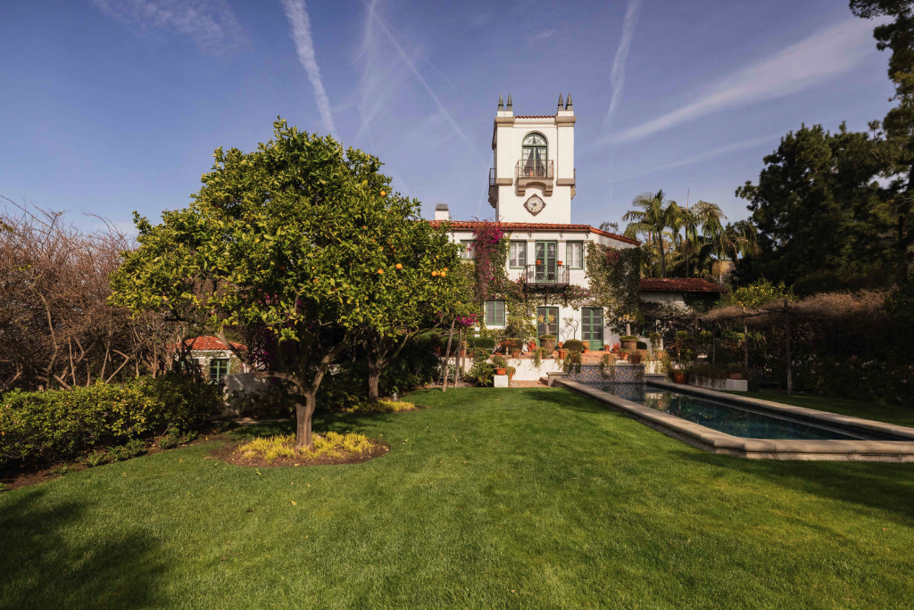 A large white house with a tower, surrounded by a green lawn, trees, and a swimming pool in the backyard.
