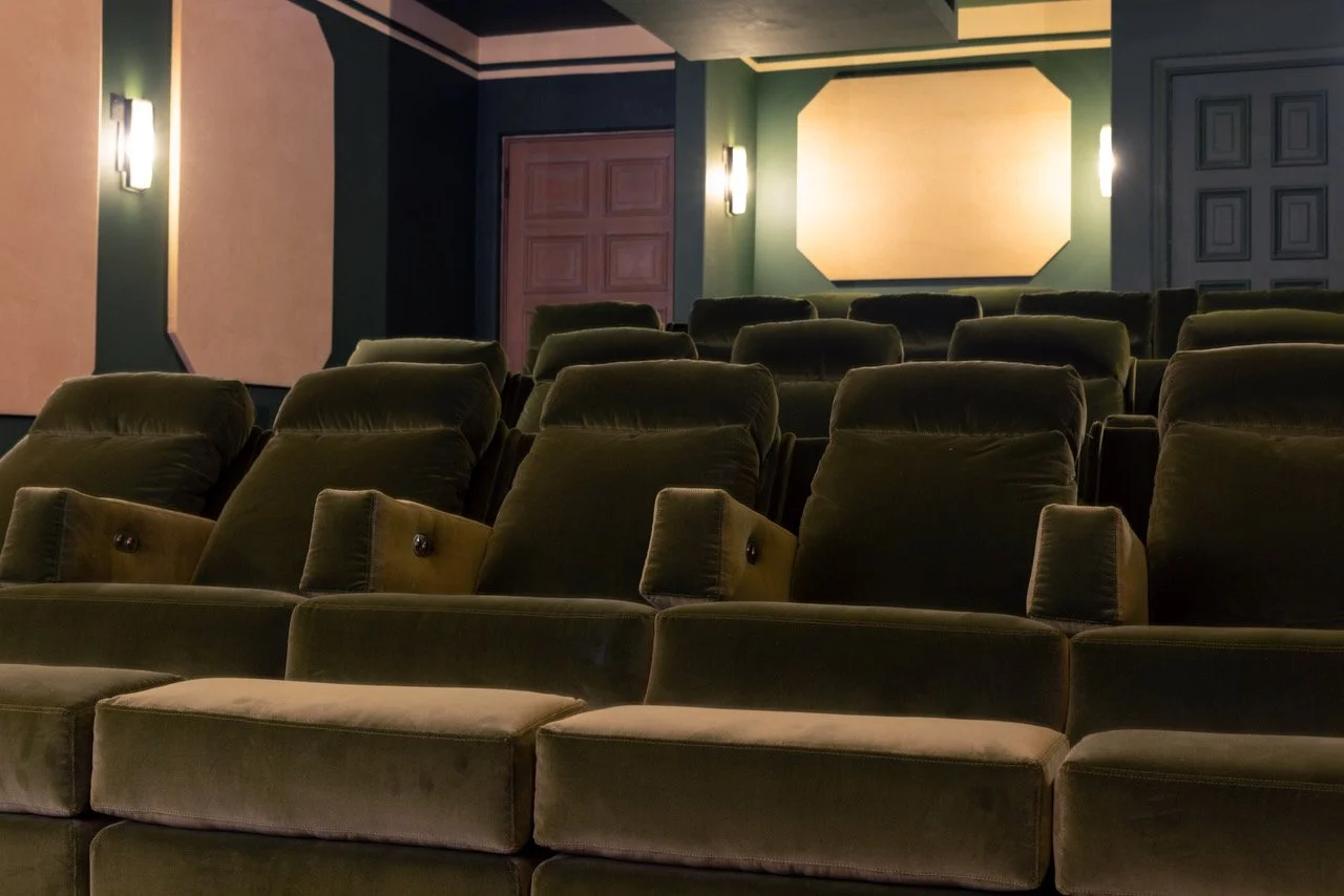 Empty movie theater with green velvet seats and dim lighting.