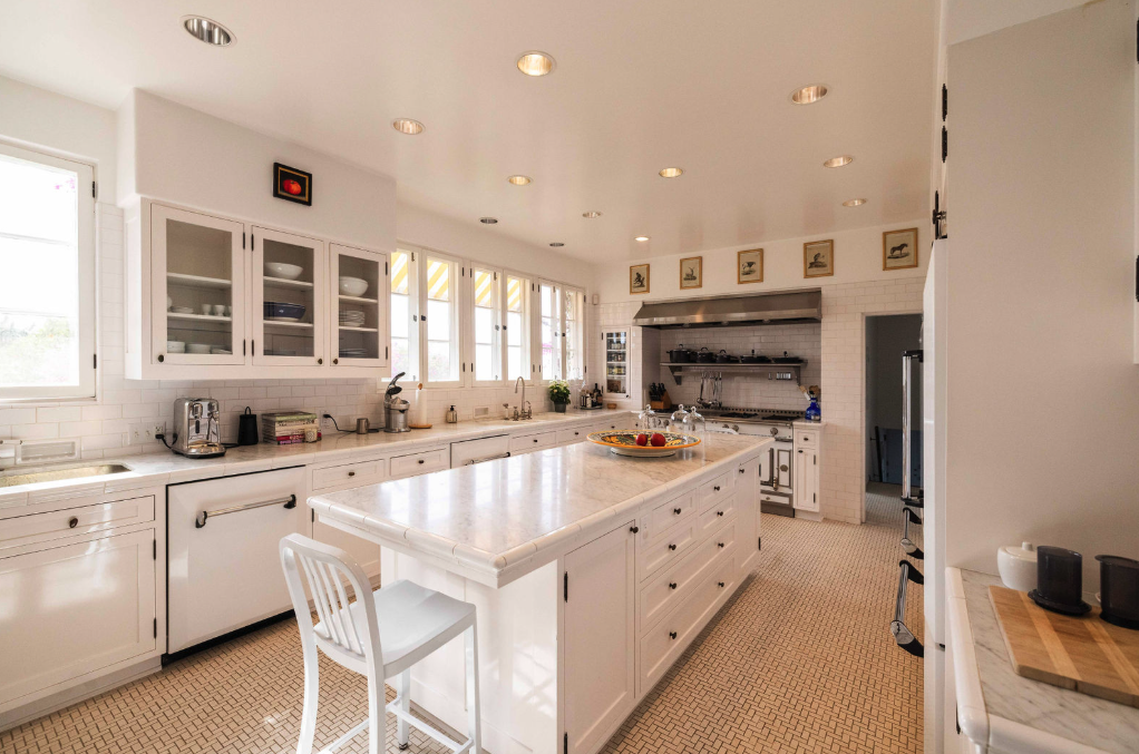 Bright white kitchen with multiple windows, white cabinets, an island, and stainless steel appliances.