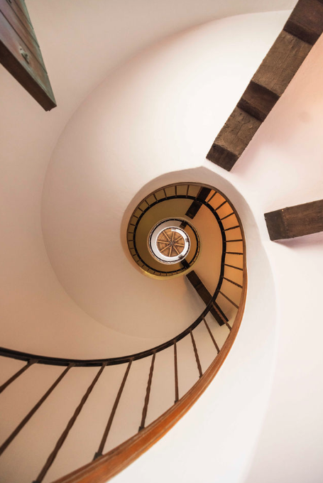 Spiral staircase viewed from above, with wooden steps and black metal railing.