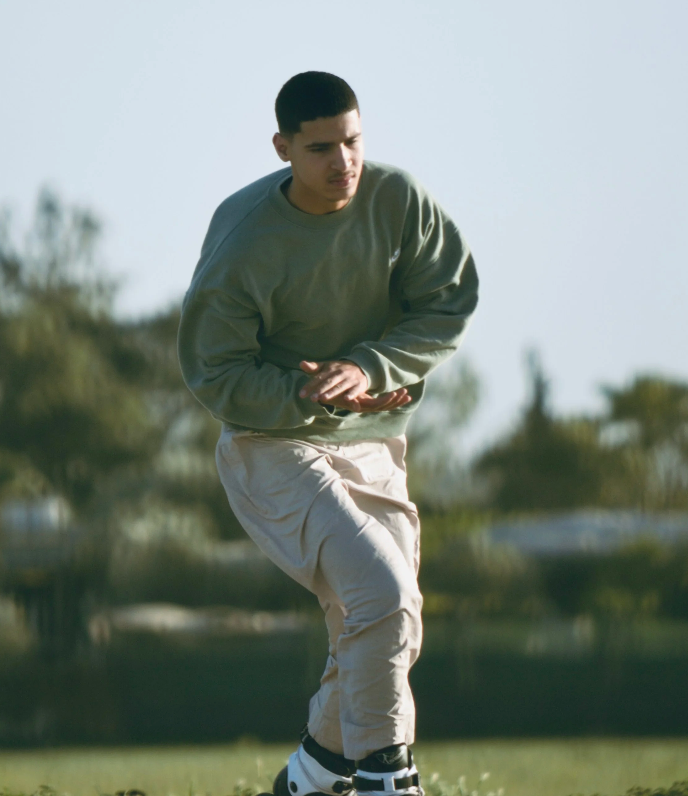 Young male golfer in a green sweatshirt and beige pants preparing to putt on a golf course with water and trees in the background.