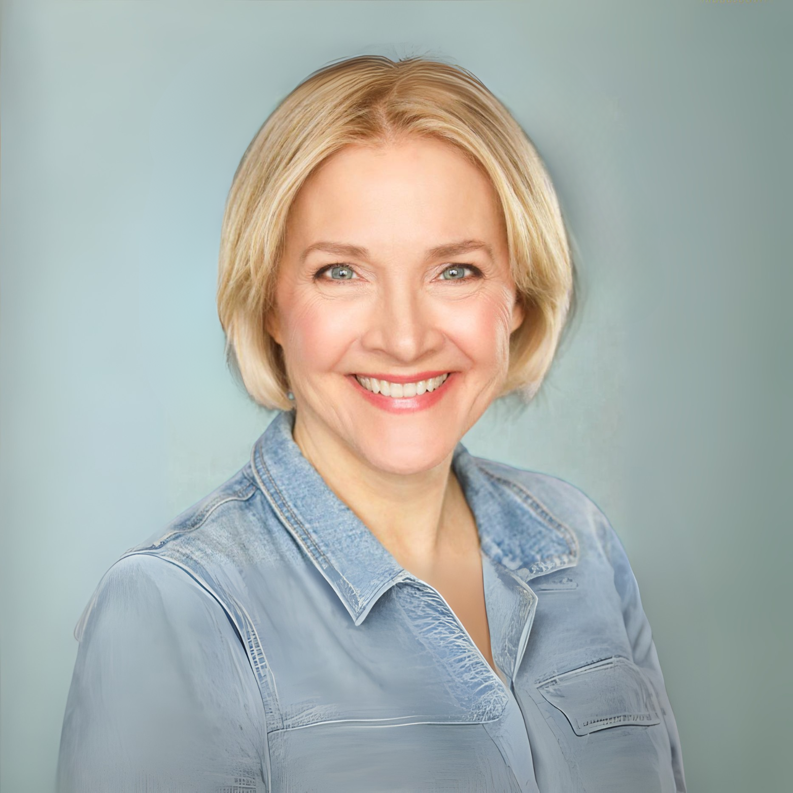 A smiling woman with blonde hair wearing a denim shirt, facing forward against a soft, neutral background.