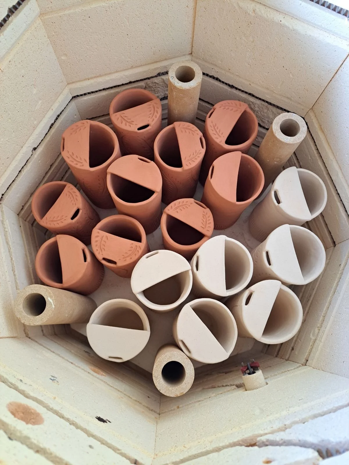 Stacked unglazed and glazed clay chimney pots and stone chimney liners inside a square brick chimney.