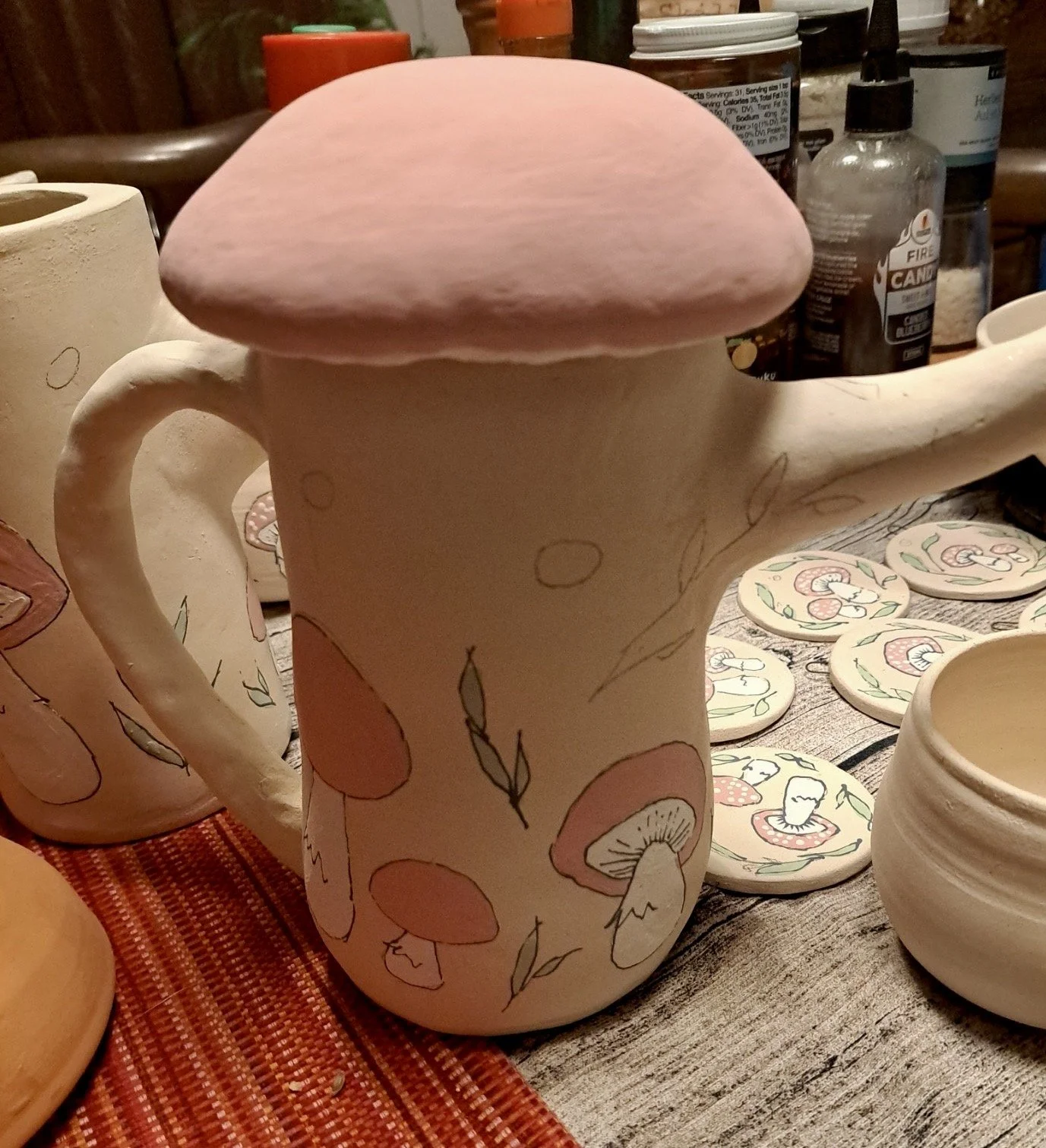 Decorative ceramic mug with mushroom and leafy patterns, topped with a pink mushroom-shaped lid.
