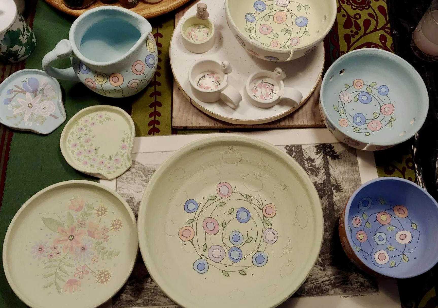 Colorful ceramic dishware with floral patterns, including bowls, cups, and a pitcher, placed on a table.