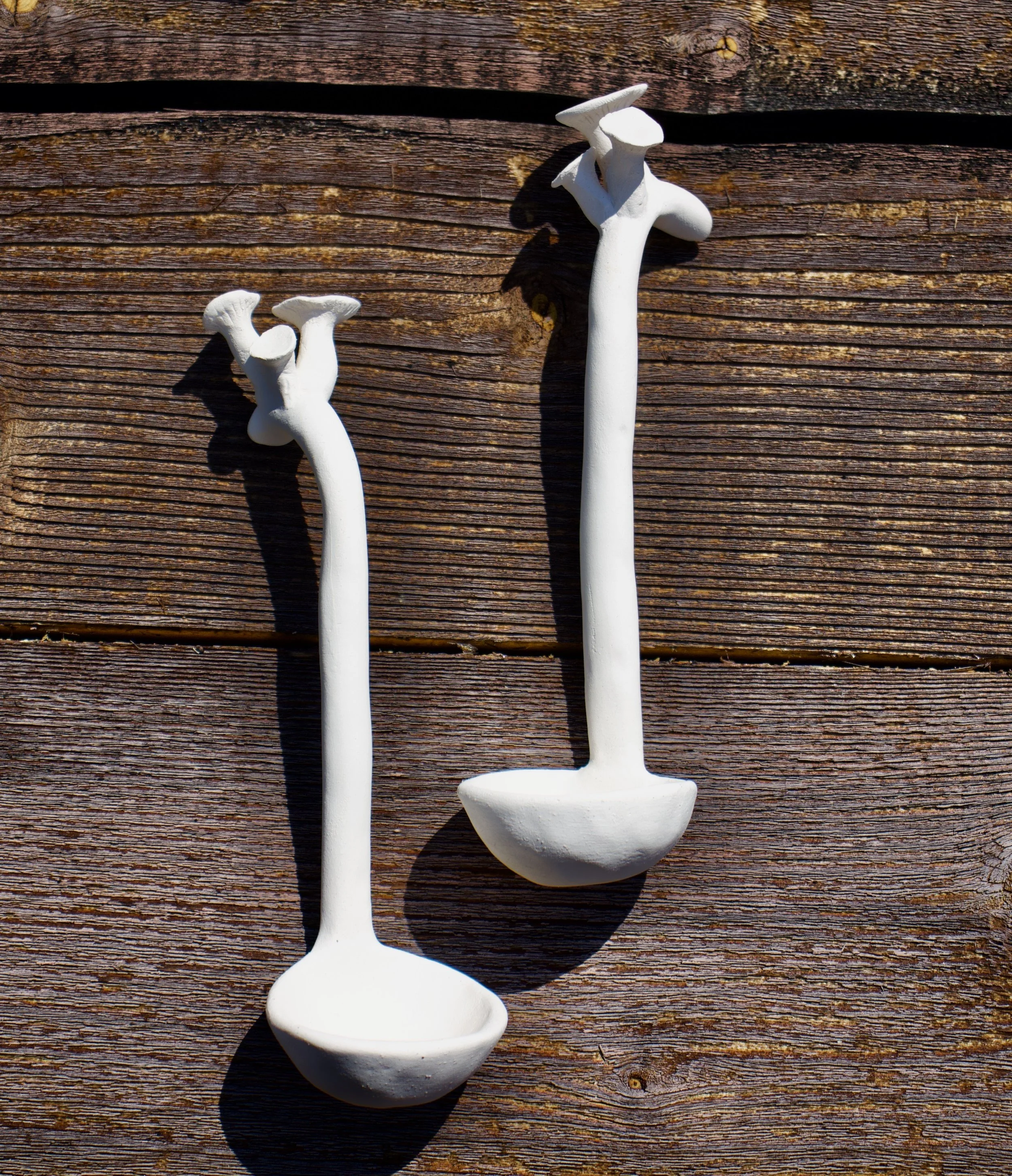 Two white vegetable or mushroom-shaped scoops placed on a wooden surface with shadows cast on it.