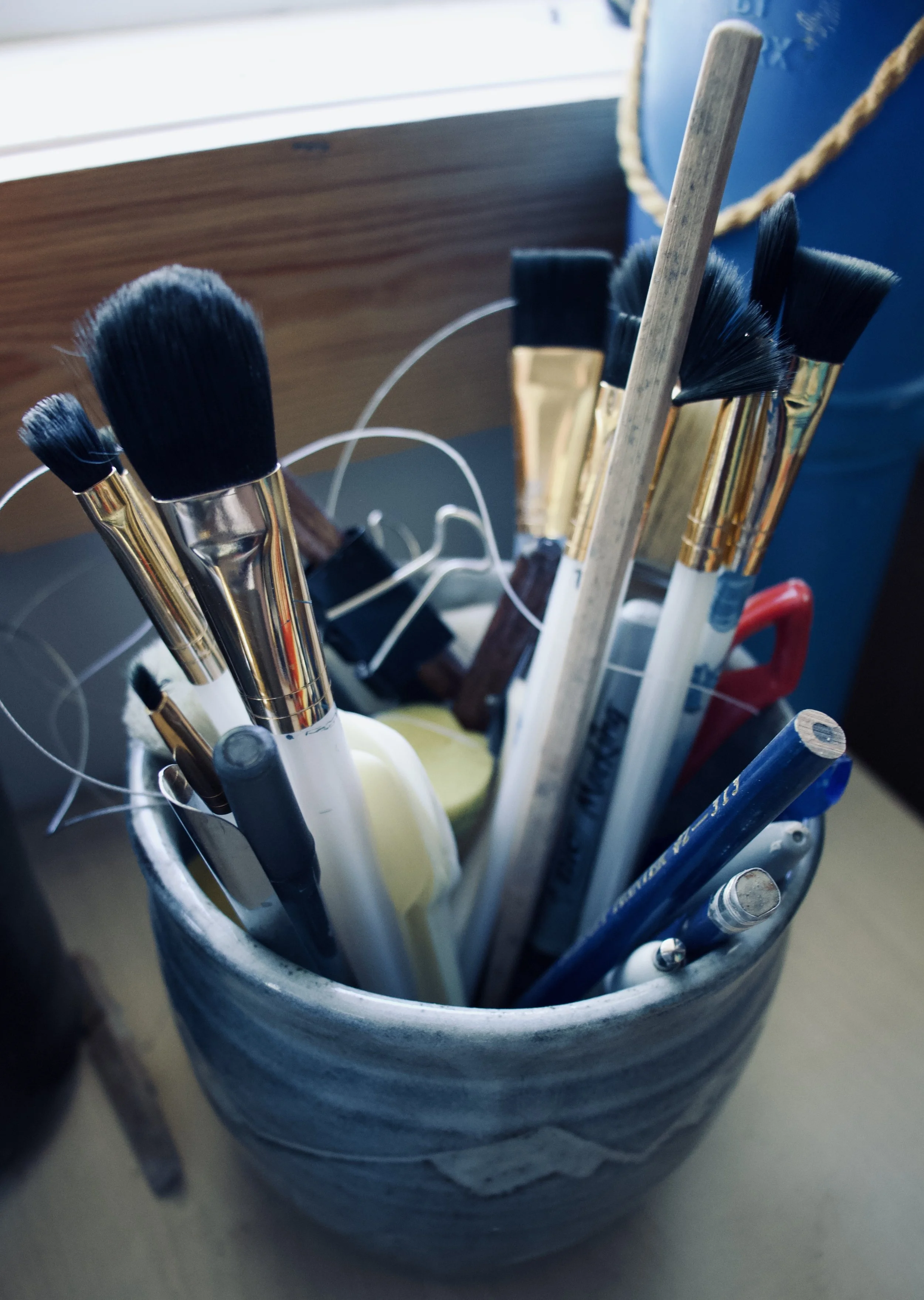 A container holding various paintbrushes, pens, and art tools.