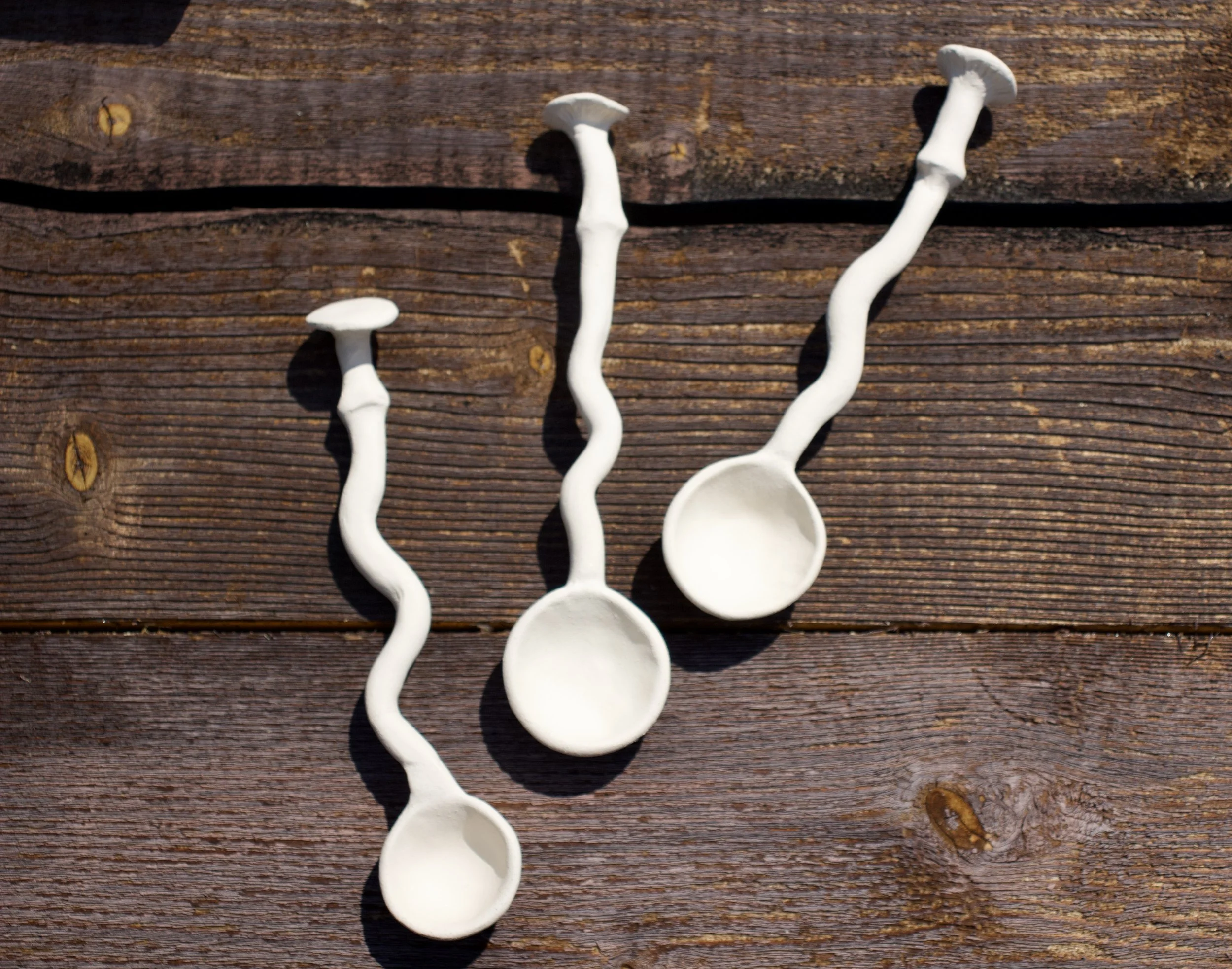 Three white ceramic spoons with wavy handles on a wooden surface