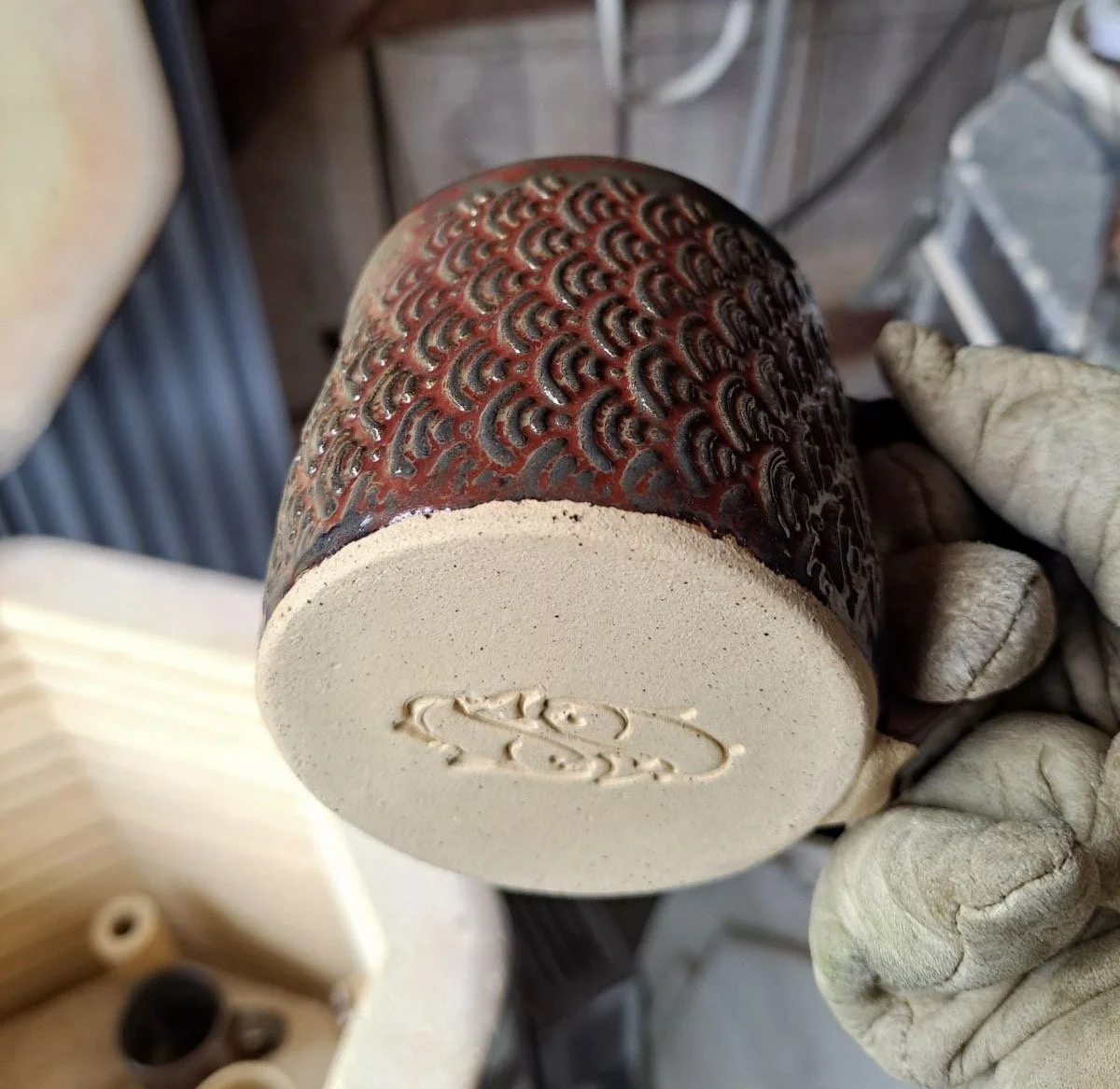 Cloth with intricate red and black pattern, titled 'Cupo' at the bottom, held in a gloved hand in a workshop setting.