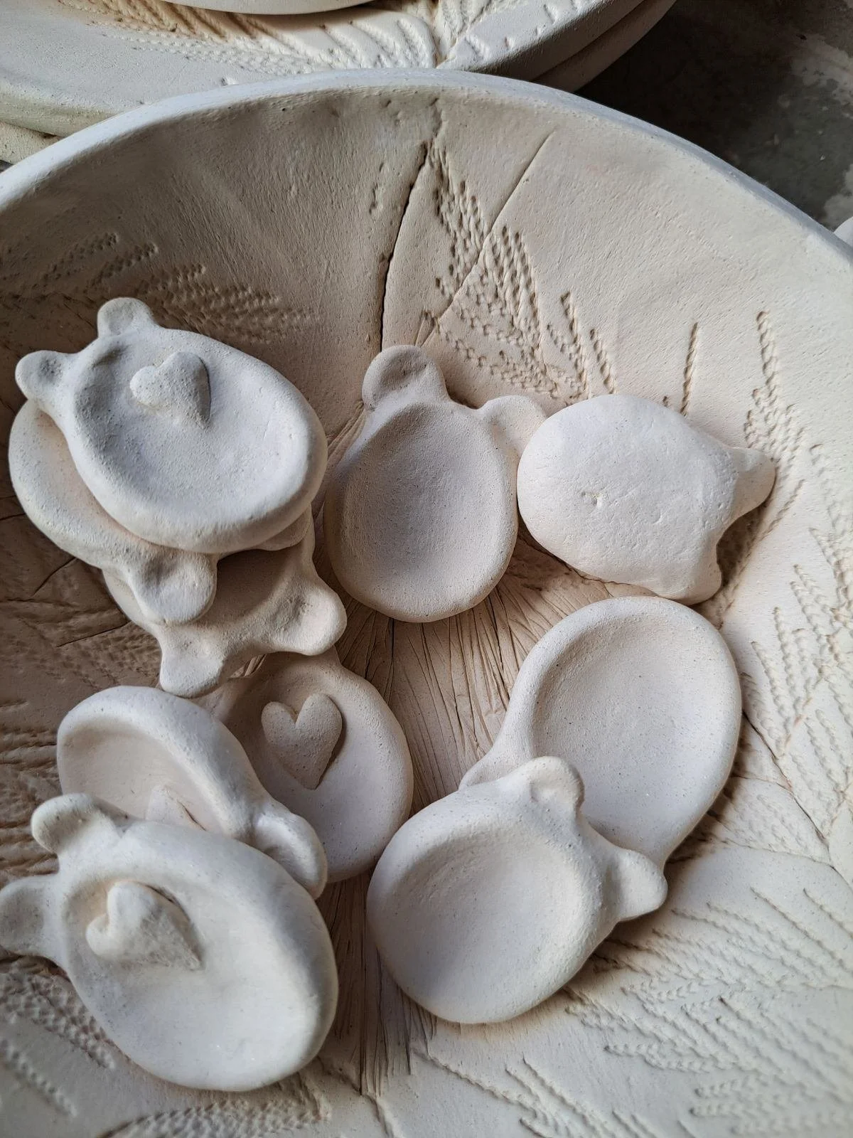 Collection of white ceramic or plaster figurines shaped like animals and hearts, inside a textured circular container.