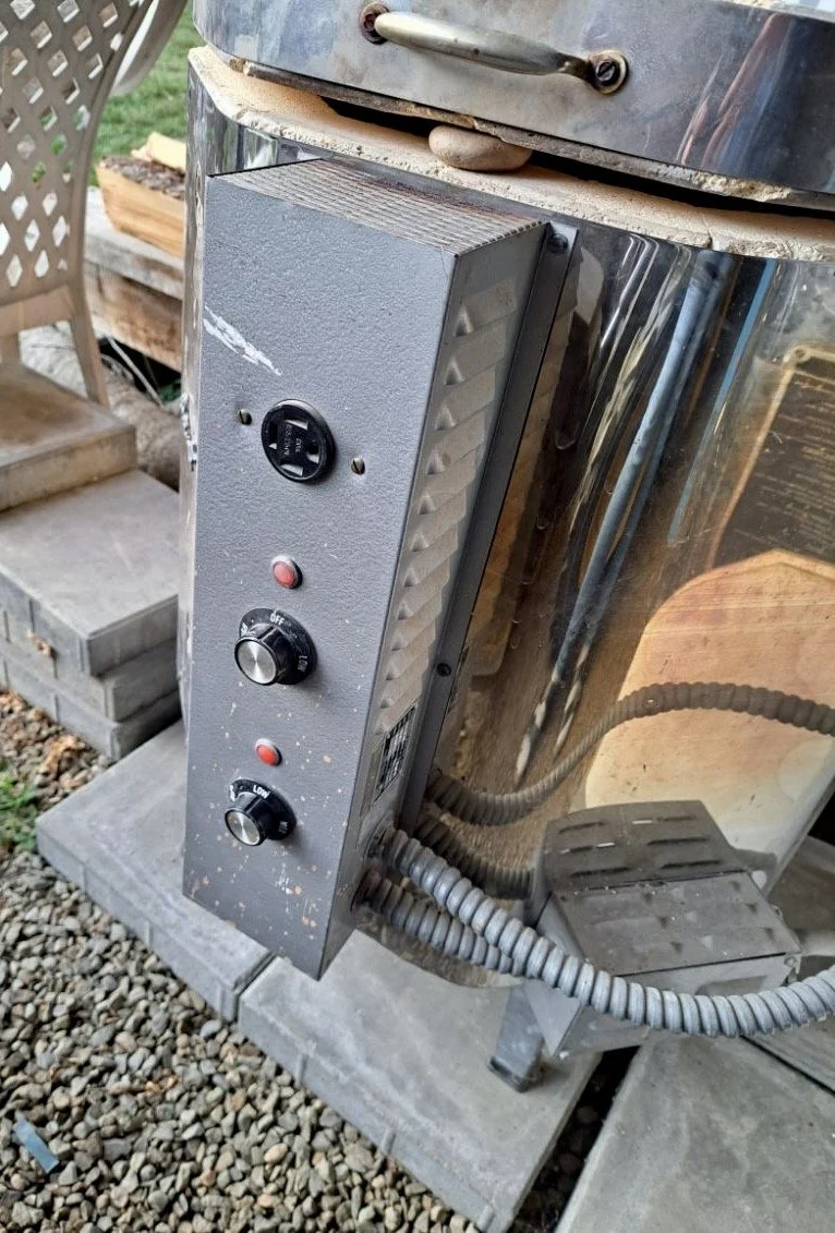 Outdoor metal smoker or grill with control knobs and electrical outlet, placed on concrete blocks.