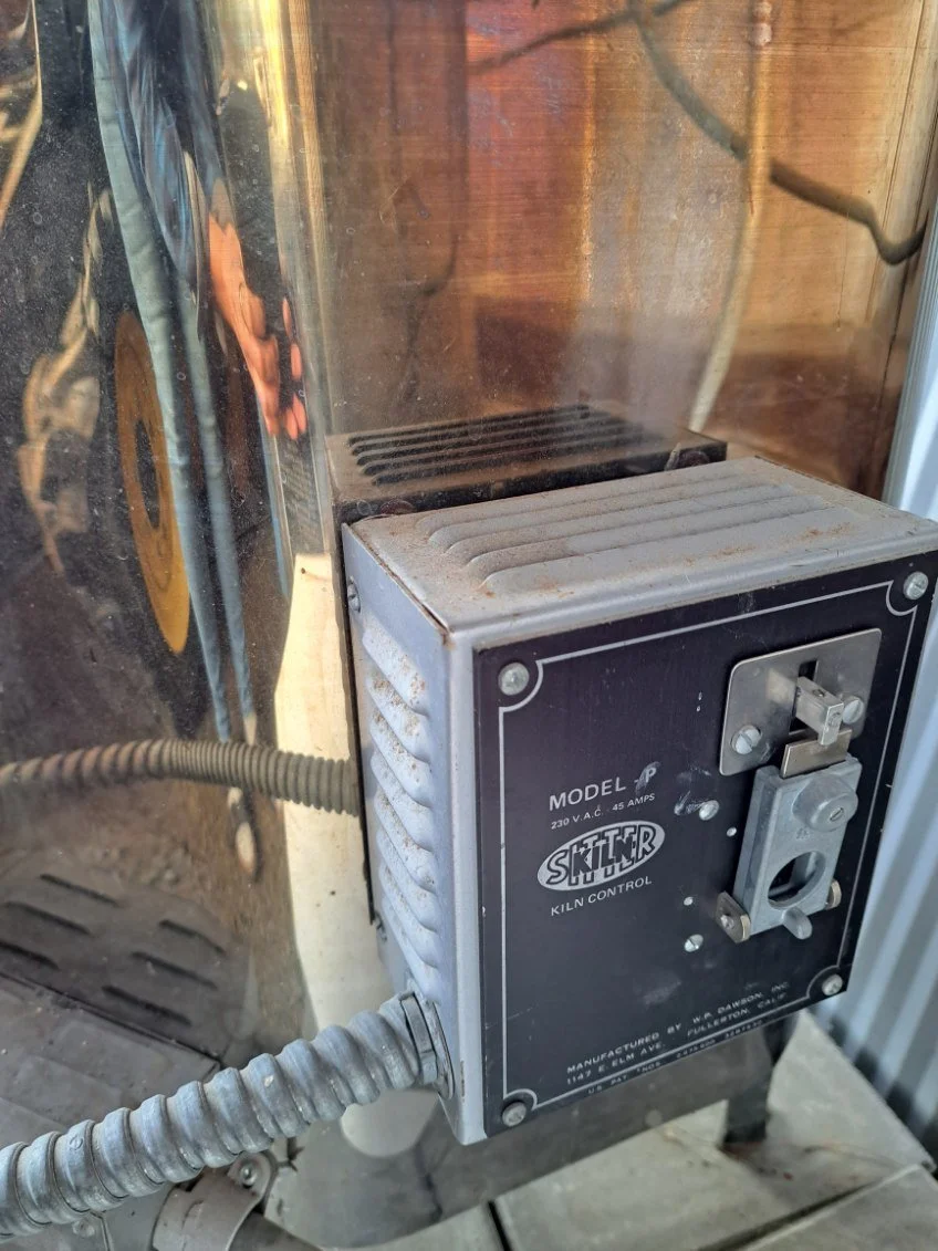 Close-up of a Skitr ceramic kiln kiln control box with a temperature dial and power switch, connected to a larger kiln.